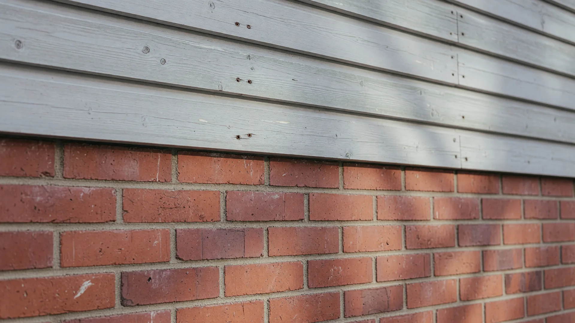 Close-up texture of brick meeting horizontal wood siding in soft daylight