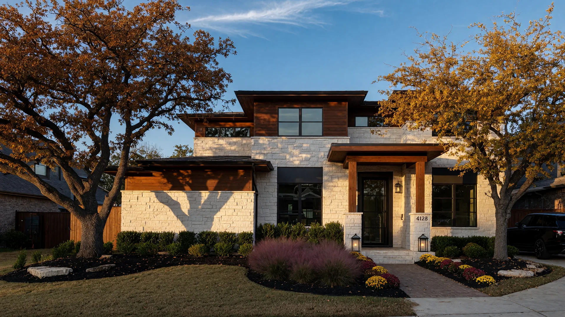 A modern North Texas home exterior at golden hour with white stone siding and dark wood trim