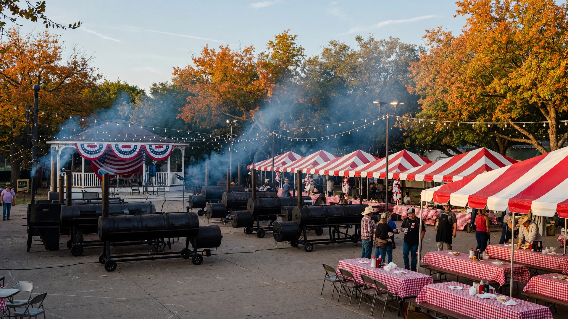 A downtown Texas beef cook-off plaza on an early October afternoon with barbecue smokers sending up thin blue smoke, red-and-white canopy tents, checkered tablecloths on picnic tables, and a gazebo stage with bunting