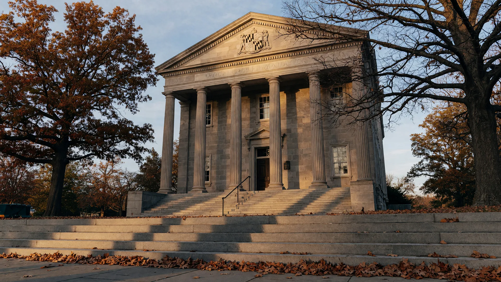 Maryland courthouse with classical columns and state seal framed by oak trees on an autumn afternoon