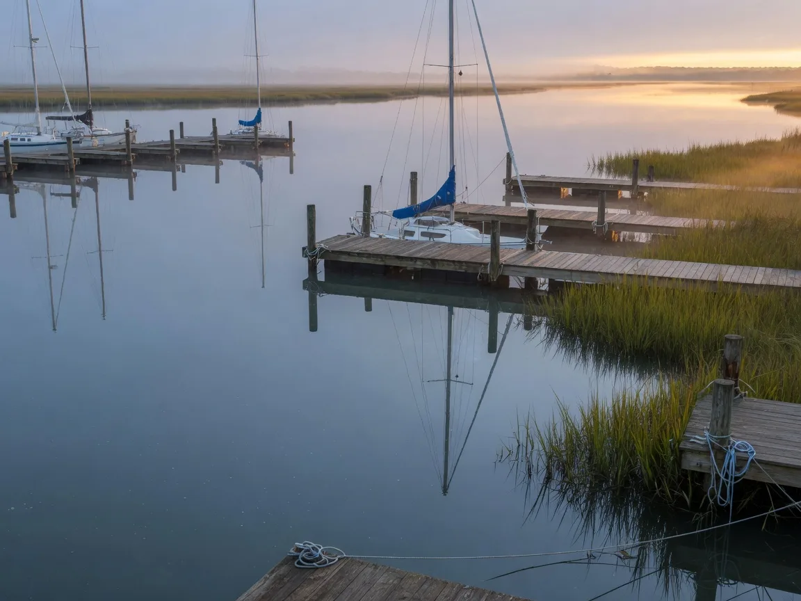 Calm marina at dawn with sailboat masts doubled in mirror-still water