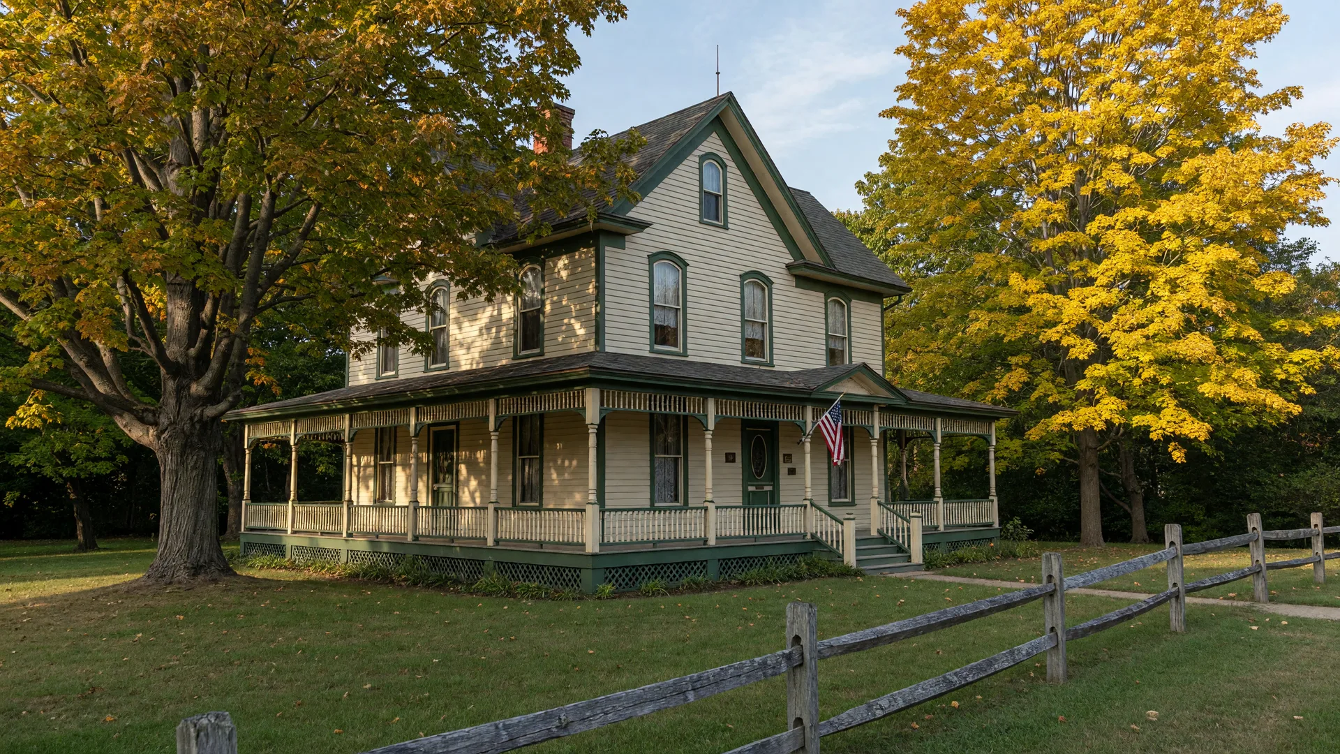 The restored 1880s Victorian farmhouse of President James A. Garfield at his historic site in Mentor Ohio, with a wraparound porch, cream and forest-green woodwork, an American flag by the entry and early-autumn maples turning gold in late-afternoon light