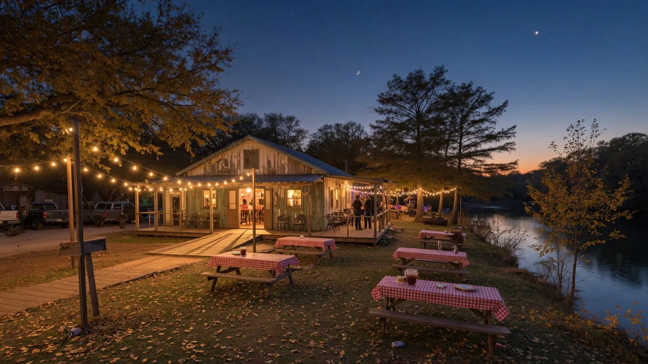 A rustic Texas Hill Country dance hall and event grounds at dusk, warm string lights over wooden porches, golden live oak leaves,and a calm river beyond