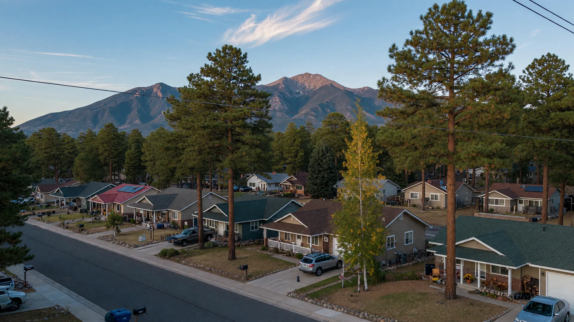 Flagstaff residential neighborhoods with pitched-roof homes among ponderosa pines and turning aspens under the San Francisco Peaks in late September light