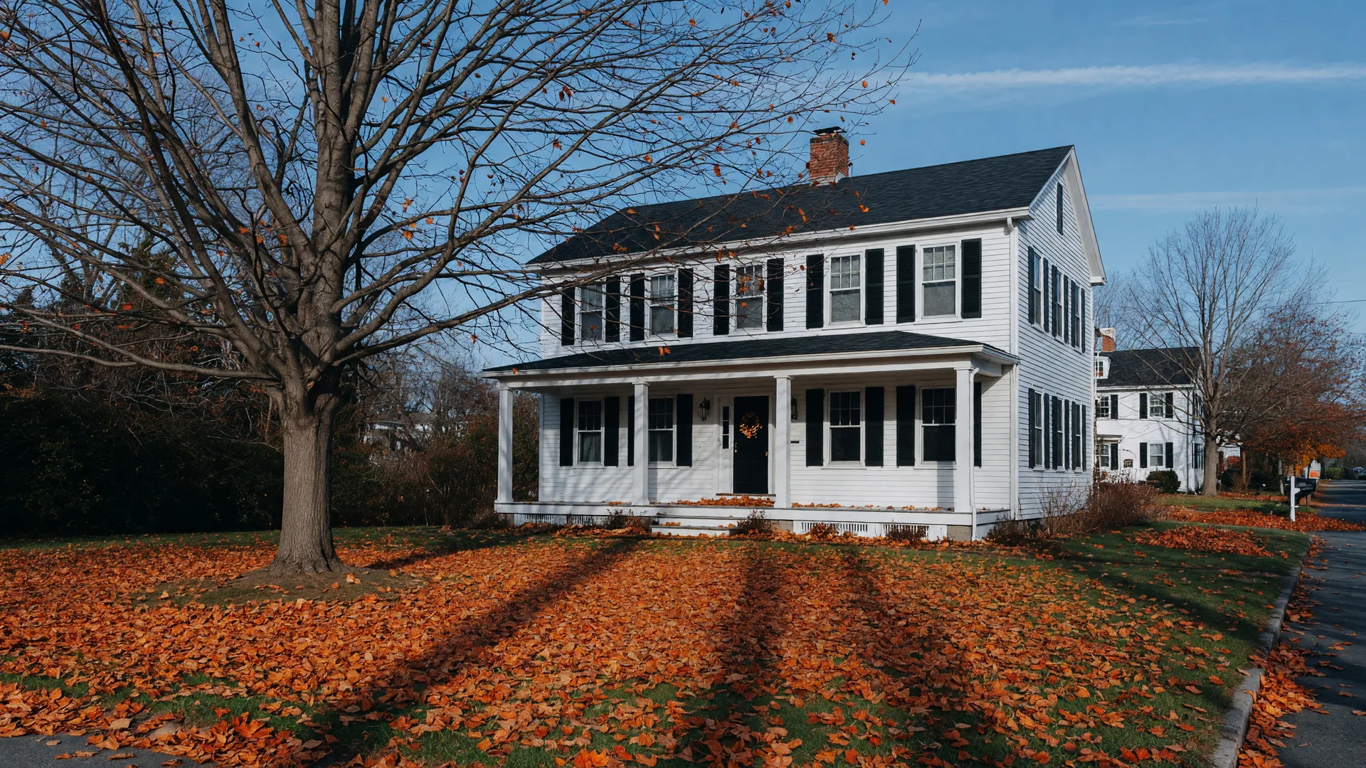 Classic white clapboard North Shore home with black shutters on a leaf-covered lawn in late November