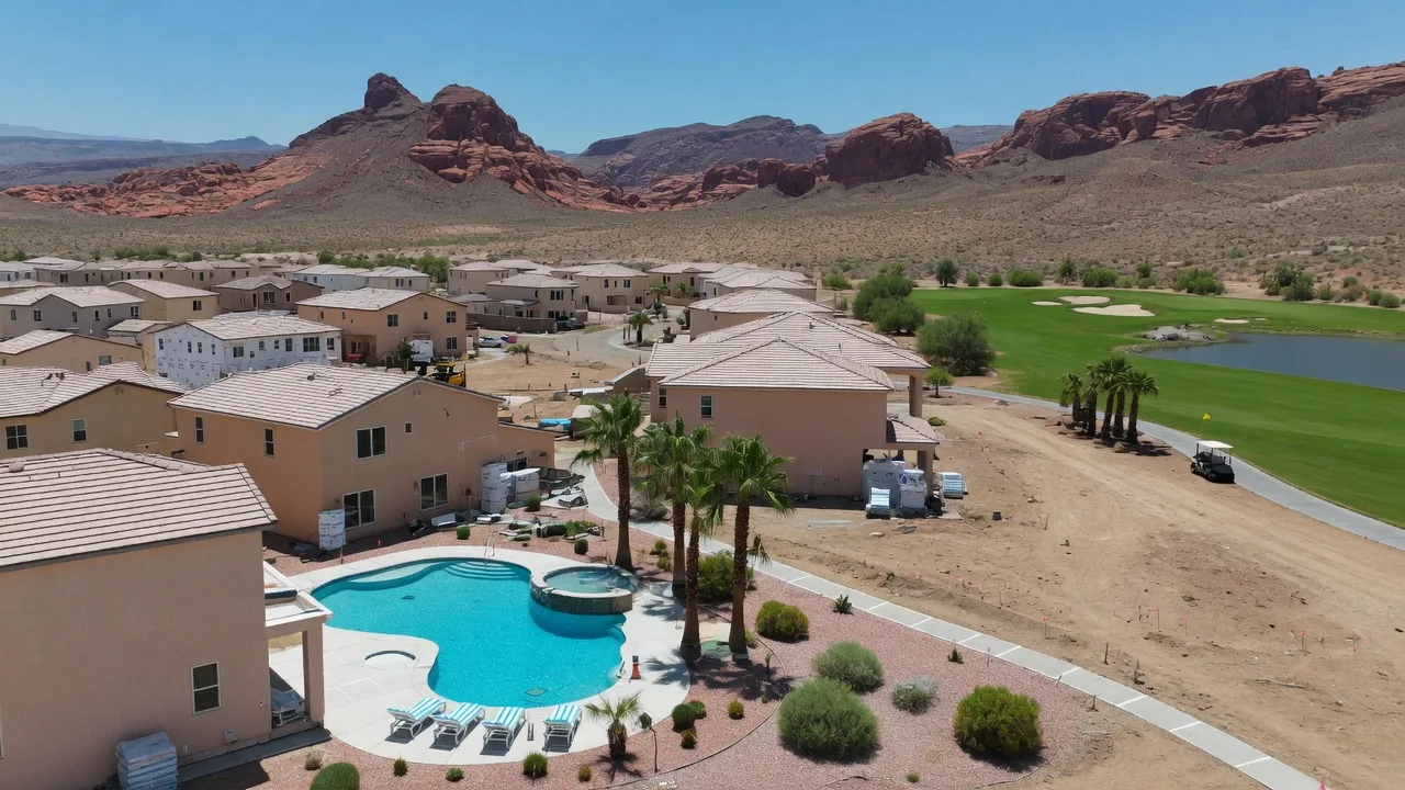 New desert-style homes with terracotta roofs and a community pool in Mesquite Nevada, with red rock mountains and golf course green in the background