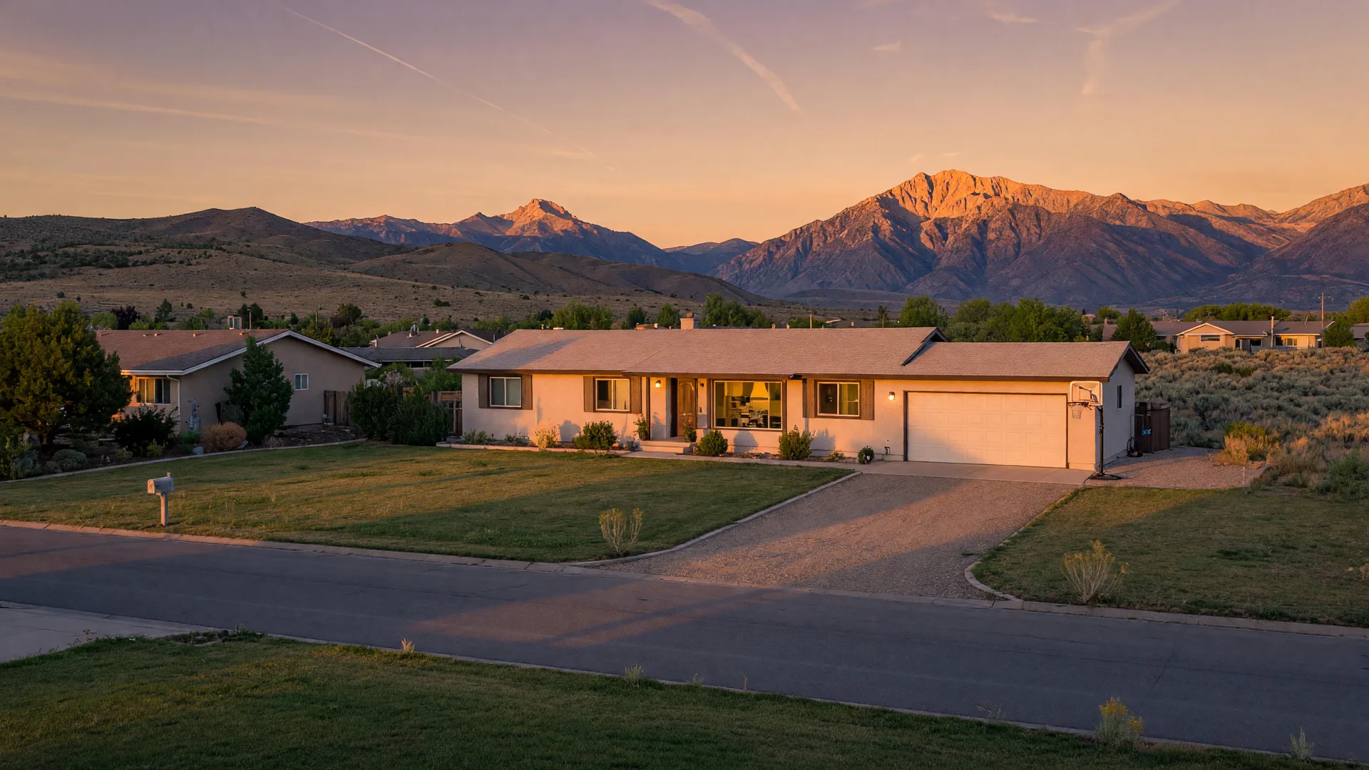 A single-story ranch home in the Carson Valley at golden hour with the Sierra Nevada glowing behind it, warm lights beginning to show in the windows.