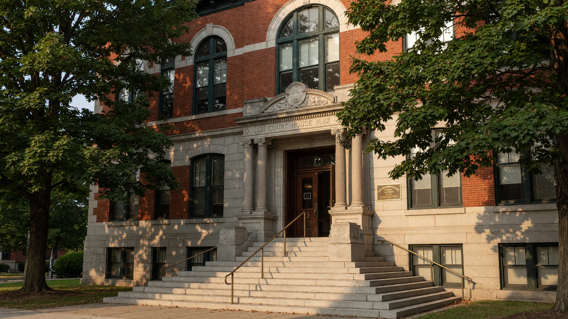 A classic Connecticut courthouse building on a warm summer afternoon with arched windows, mature oak trees, and a welcoming entrance