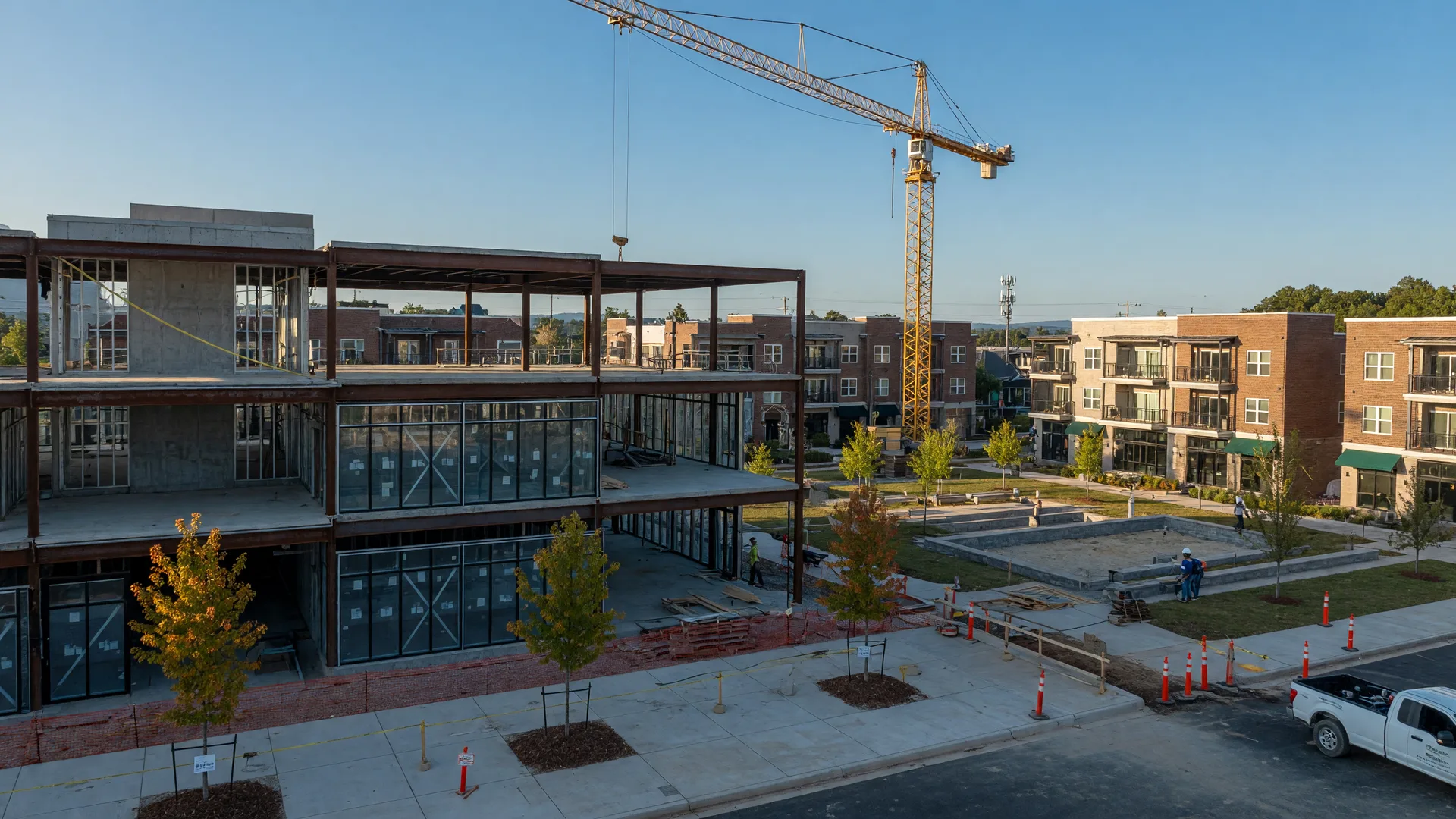 A modern mixed-use development under construction in south Huntersville, with steel and glass framing rising beside a planned pedestrian village core on a clear early-fall afternoon