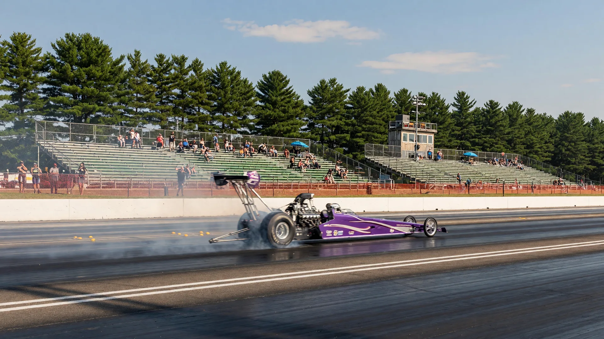 Purple dragster launching down a Minnesota raceway strip on a hot August afternoon with heat shimmer and grandstands beyond