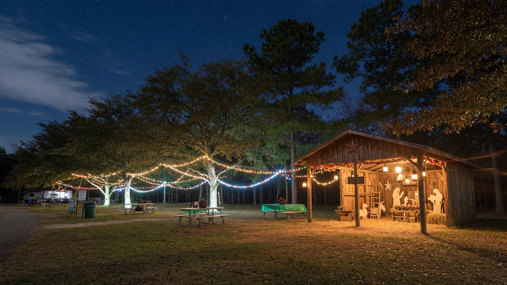 A Texas state park campground at night in December with campsites strung with twinkling holiday lights and a warm lantern-lit wooden stable