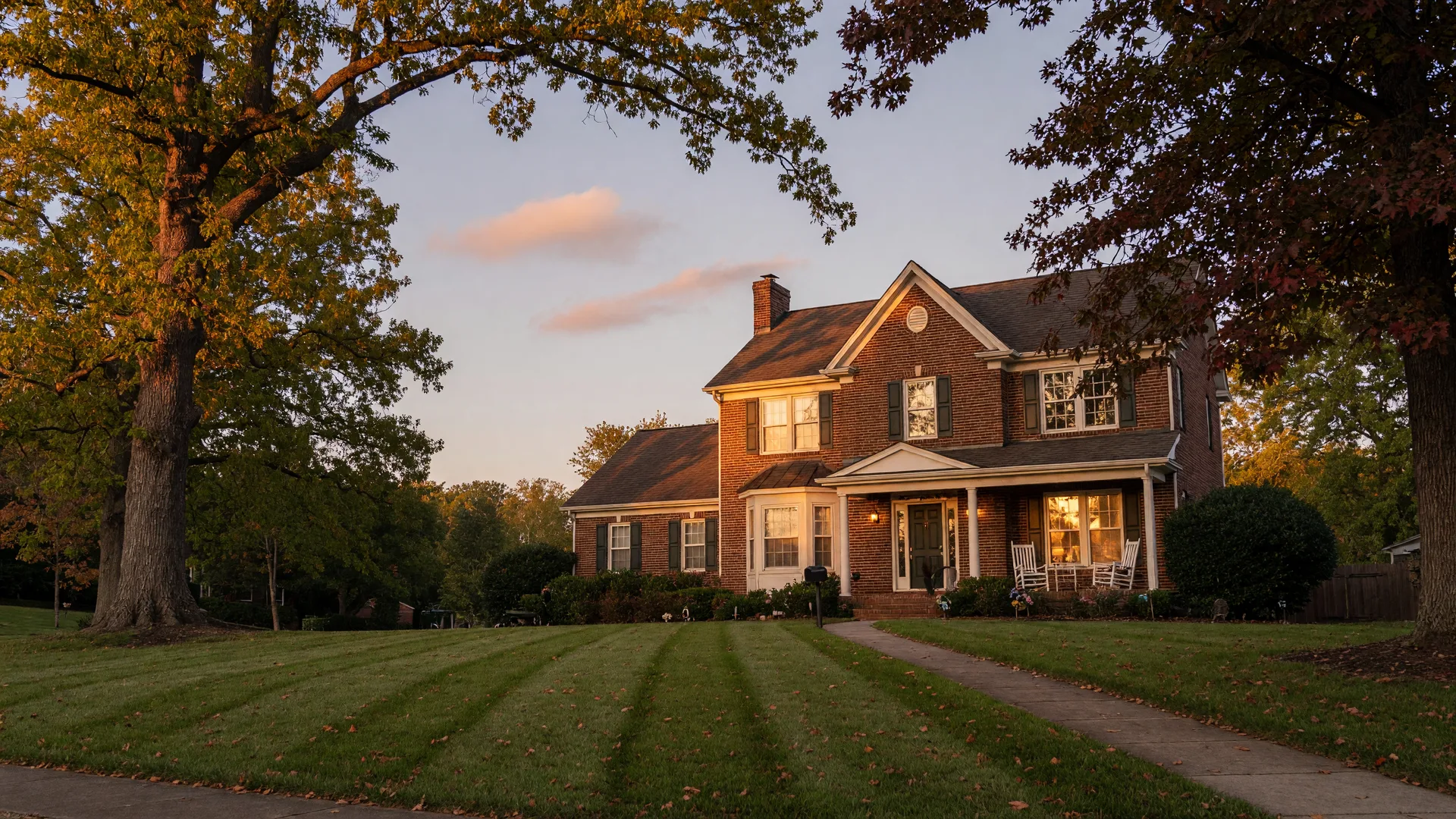 Brick suburban home in Knoxville at golden hour with warm window lights and mature oak trees
