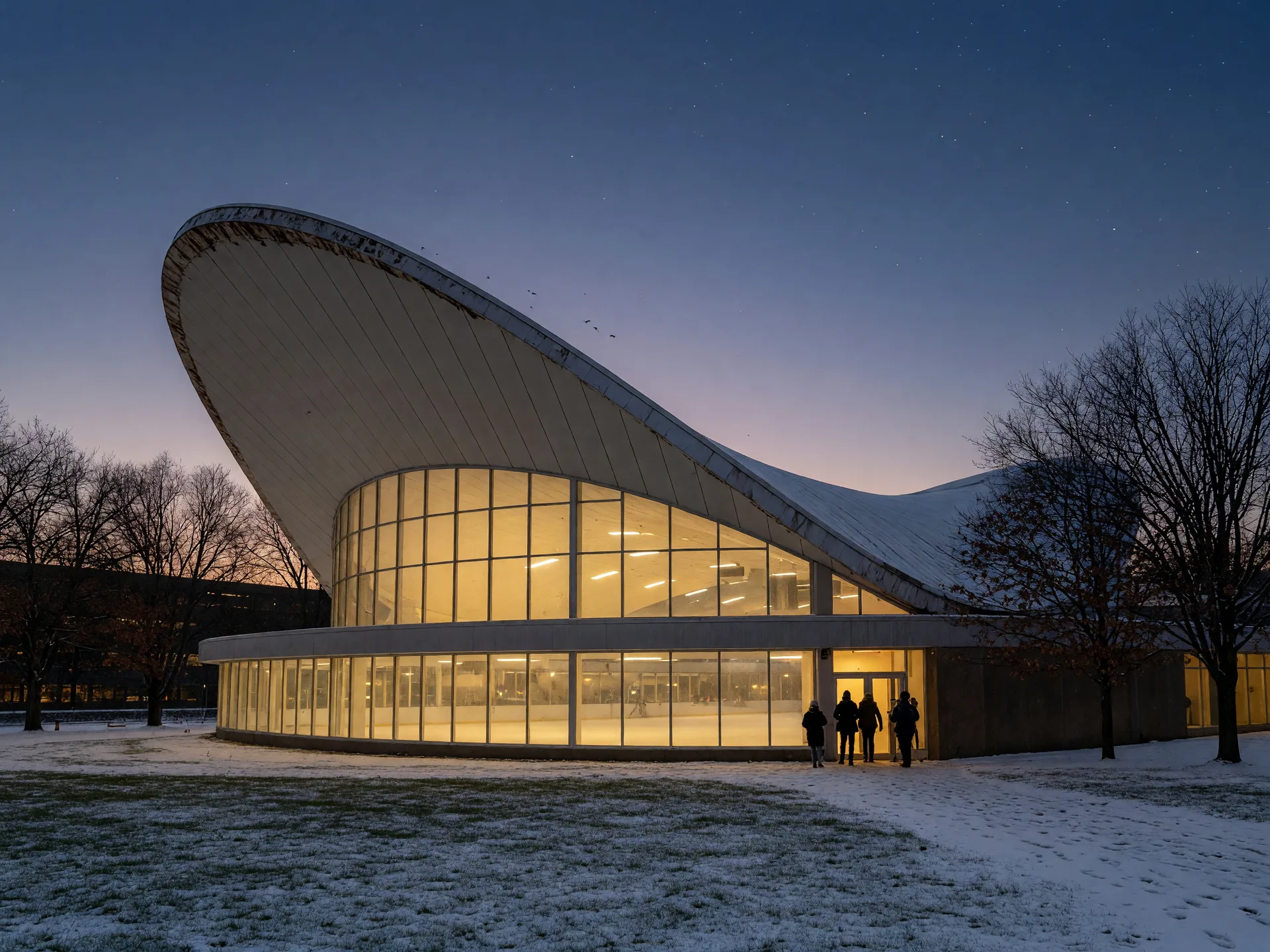 The sweeping curved white roofline of Ingalls Rink, the Yale Whale, glowing warmly at dusk with a dusting of snow on the ground