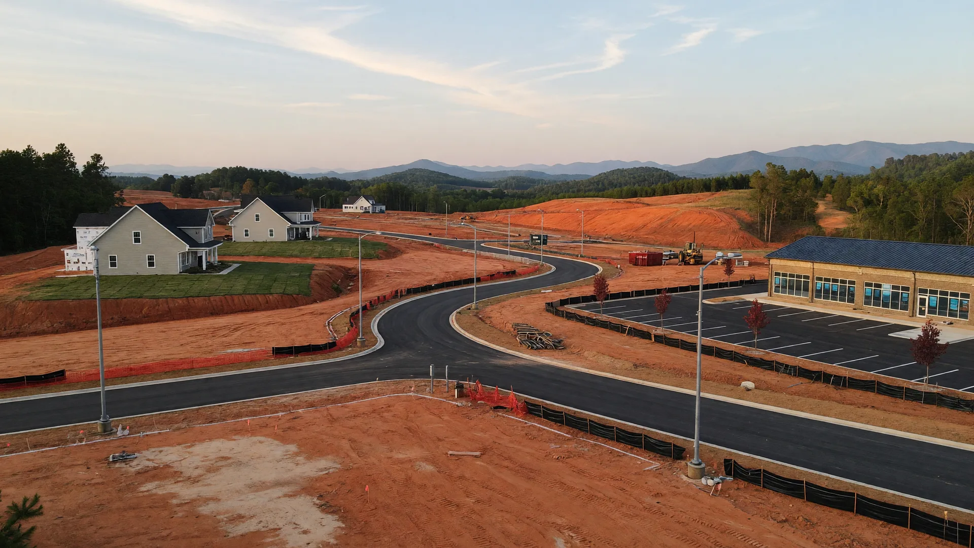 Graded red-clay ground and new homes rising along a rural corridor in northeast Georgia's rolling foothills
