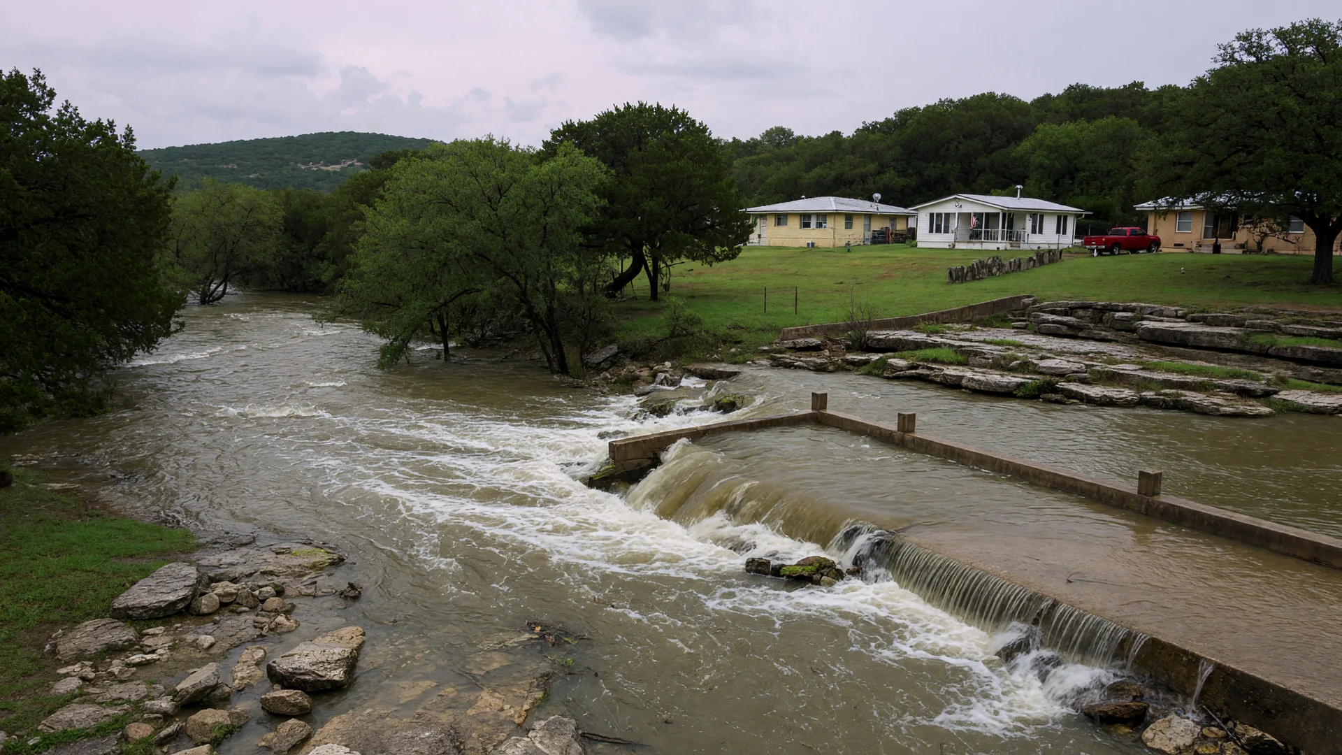 Rain-swollen Hill Country creek rushing over a low-water crossing near homes on the bank