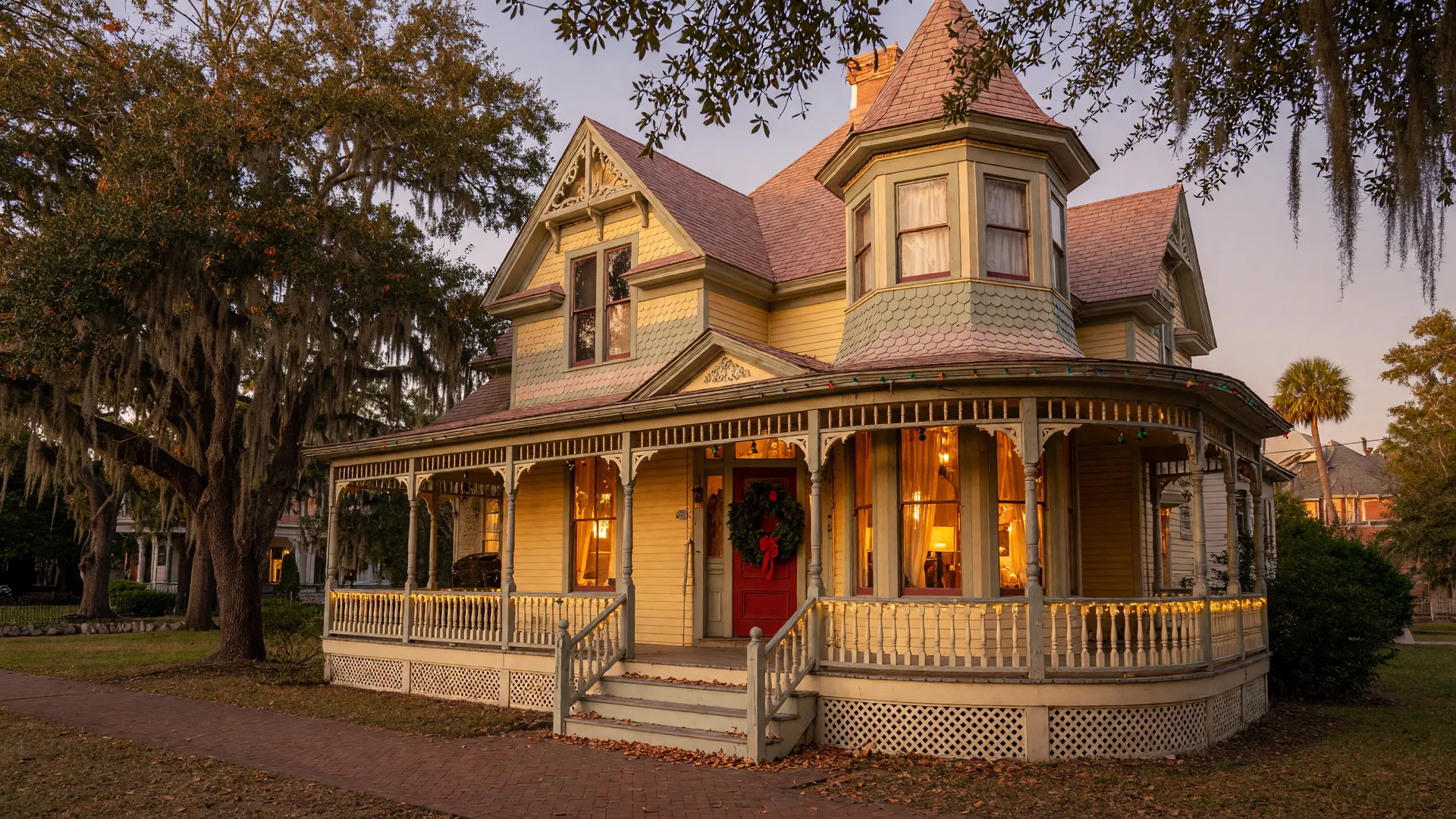 A Queen Anne Victorian home in Pensacola's North Hill district on a late November afternoon, evergreen wreath on the front door, warm window light, live oaks draped in Spanish moss.