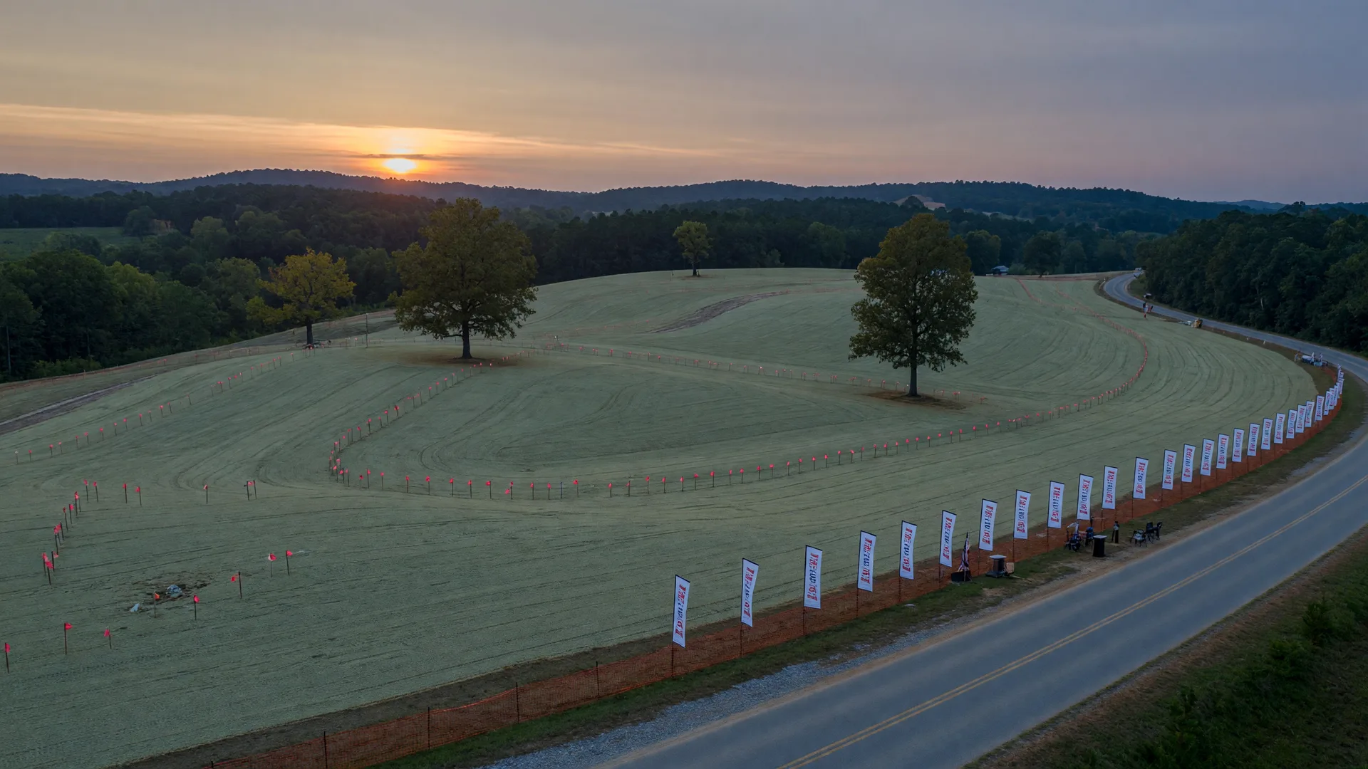 A cleared, surveyed master-plan site with a construction line along a rural road and distant forested ridges in eastern Gwinnett County at dusk