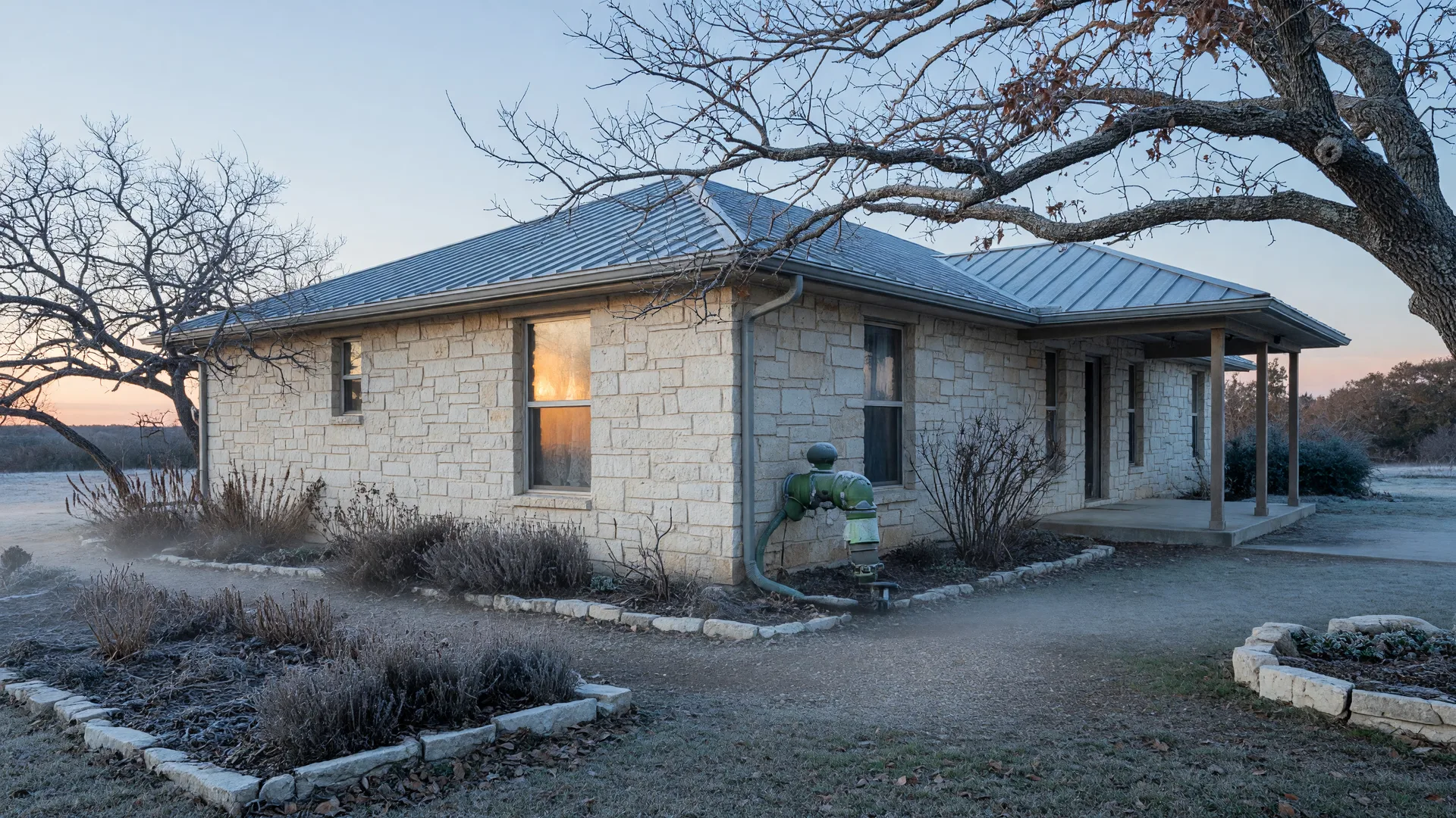 Winterizing a San Antonio home: a Texas Hill Country stone house at frosty winter dawn with a covered foam faucet insulator on the exterior hose bib and frost on the roof, ready before the first freeze