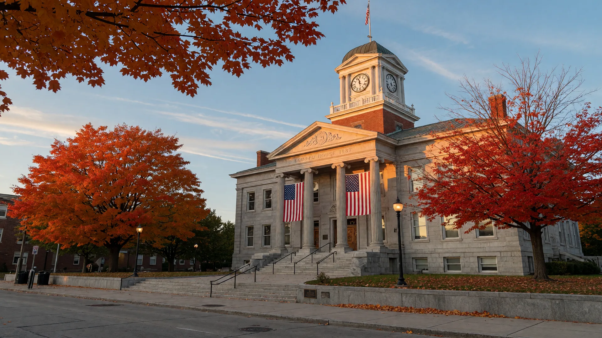 A stately Pennsylvania county courthouse with a clock tower and American flags, framed by maple trees in peak fall color, representing county government and property tax administration in the Lehigh Valley