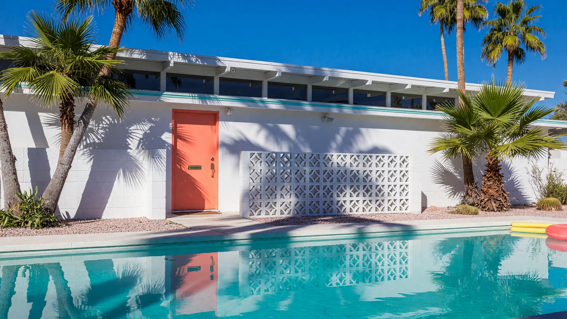 Mid-century modern Phoenix-area home with coral door, palms, and turquoise pool