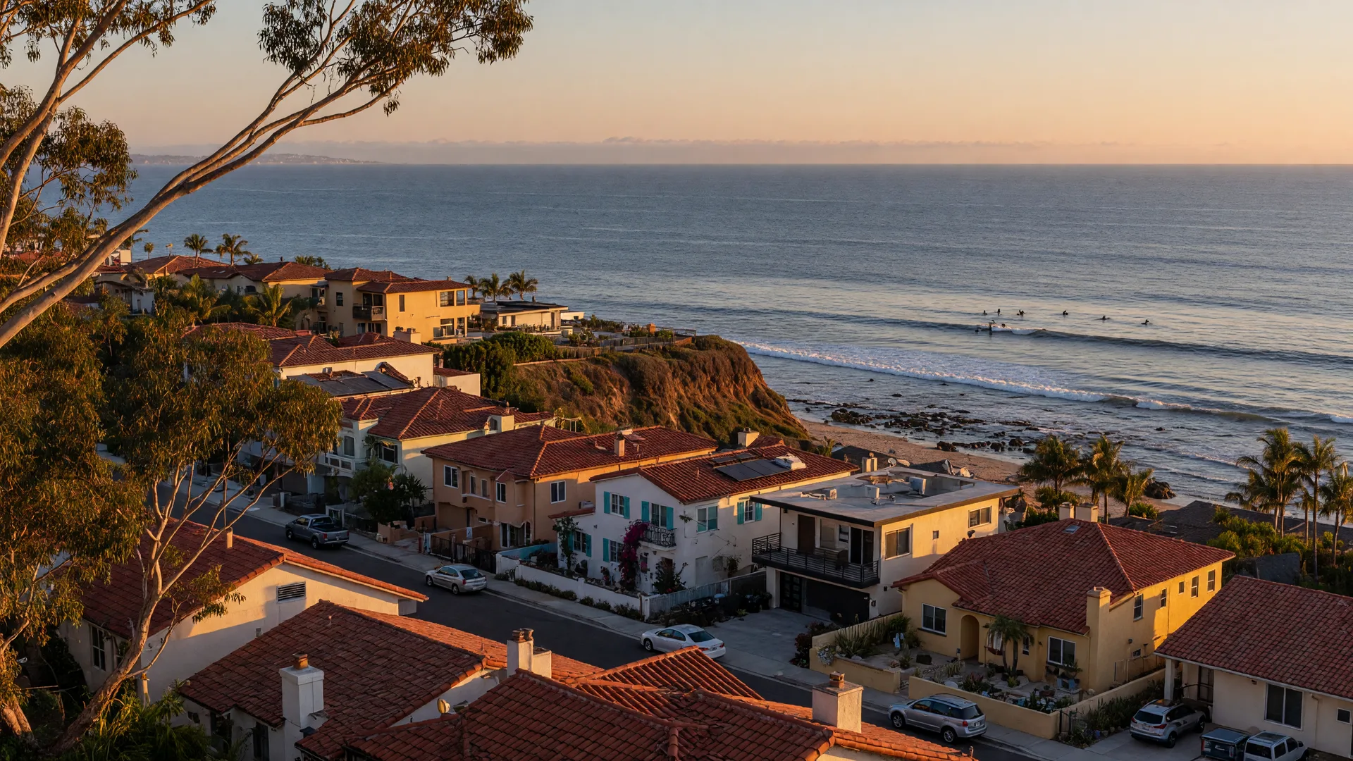 Aerial-style view of a coastal San Diego bluff neighborhood at golden hour, Spanish and modern homes with terracotta roofs above the Pacific surf line