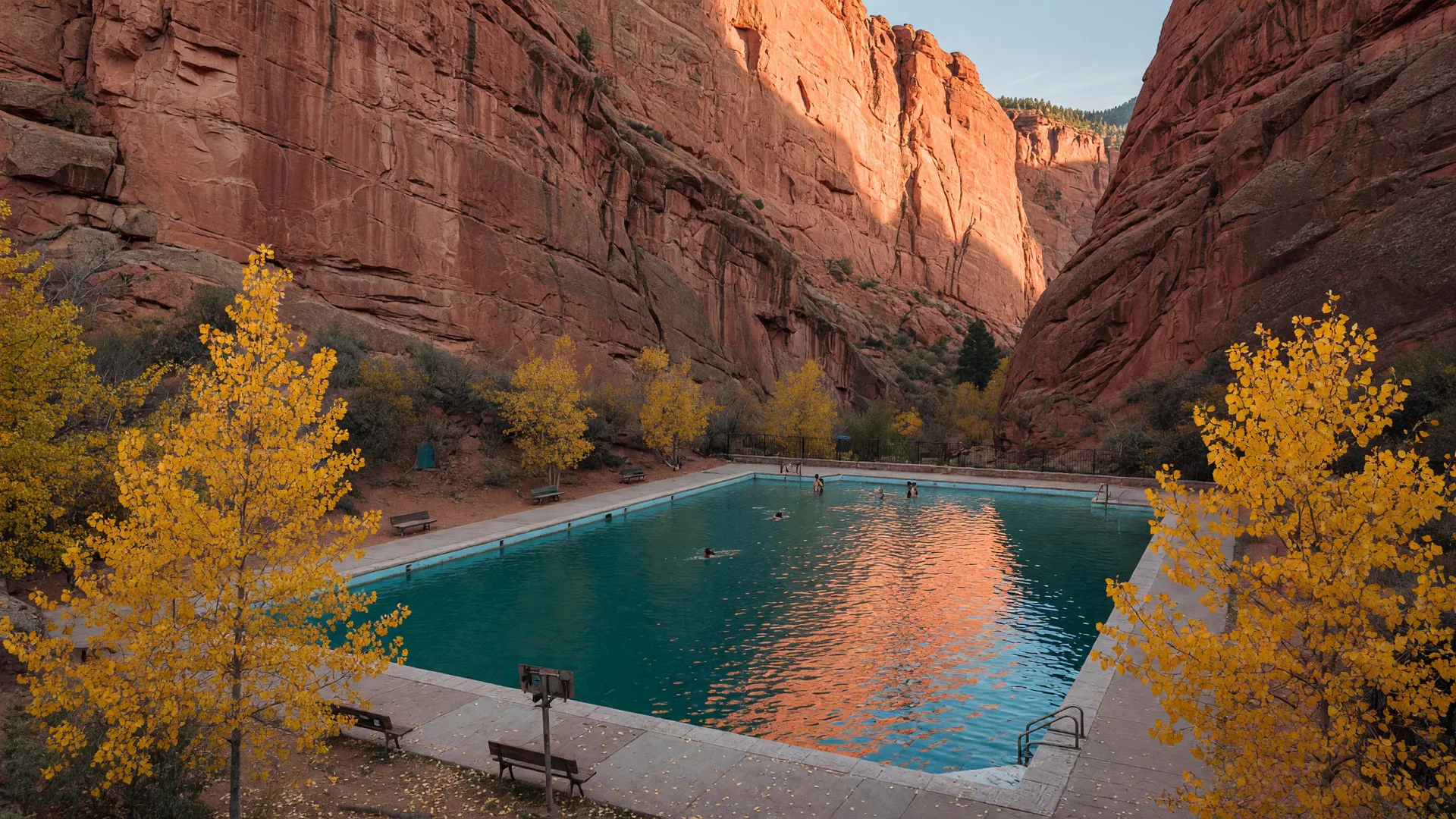 The turquoise Eldorado Springs Pool glistening below towering golden sandstone cliffs of Eldorado Canyon at golden hour