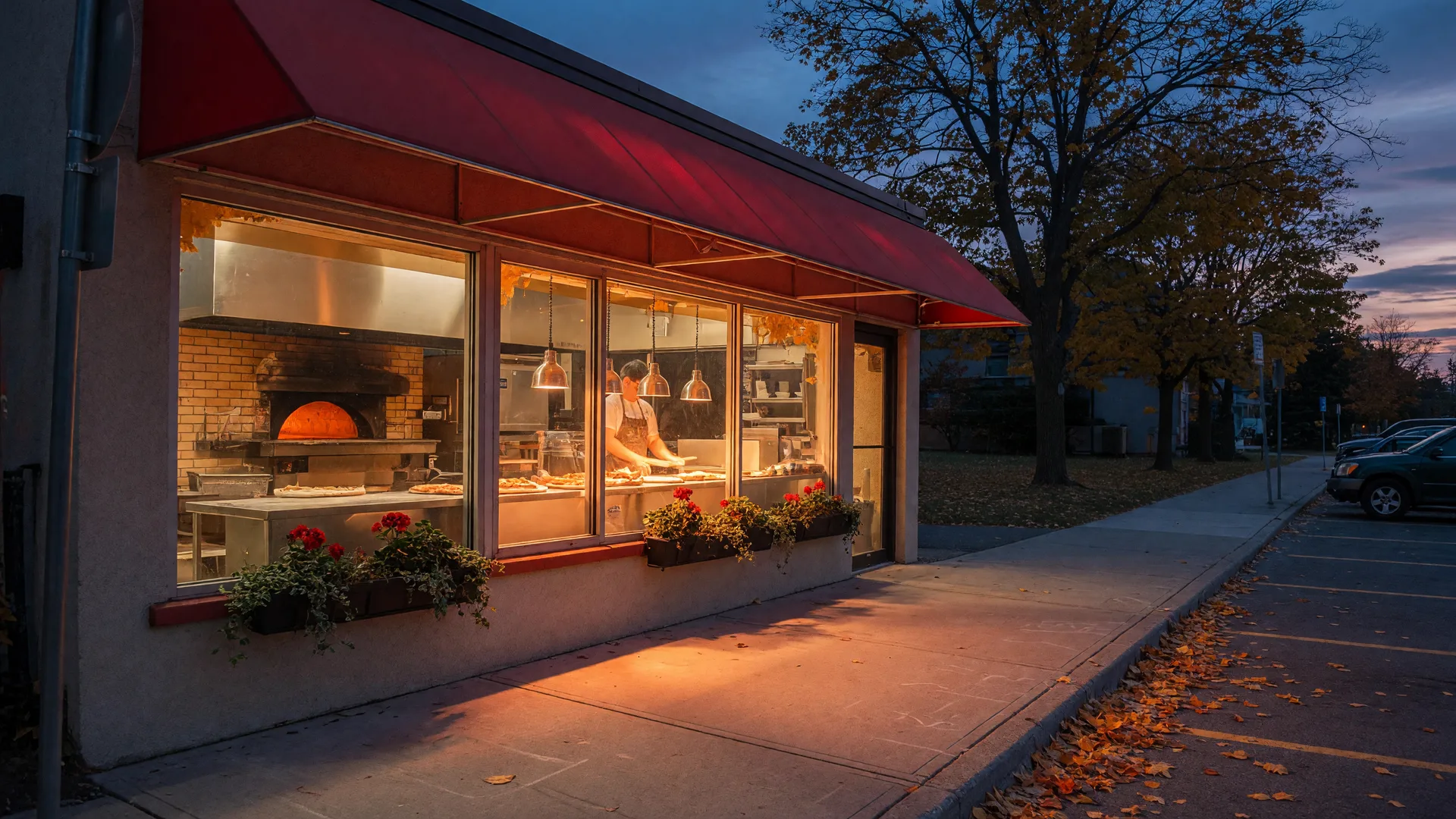 A warm neighbourhood Italian pizzeria storefront on a commercial street in Ajax, Ontario at autumn dusk, with a red awning and glowing front windows