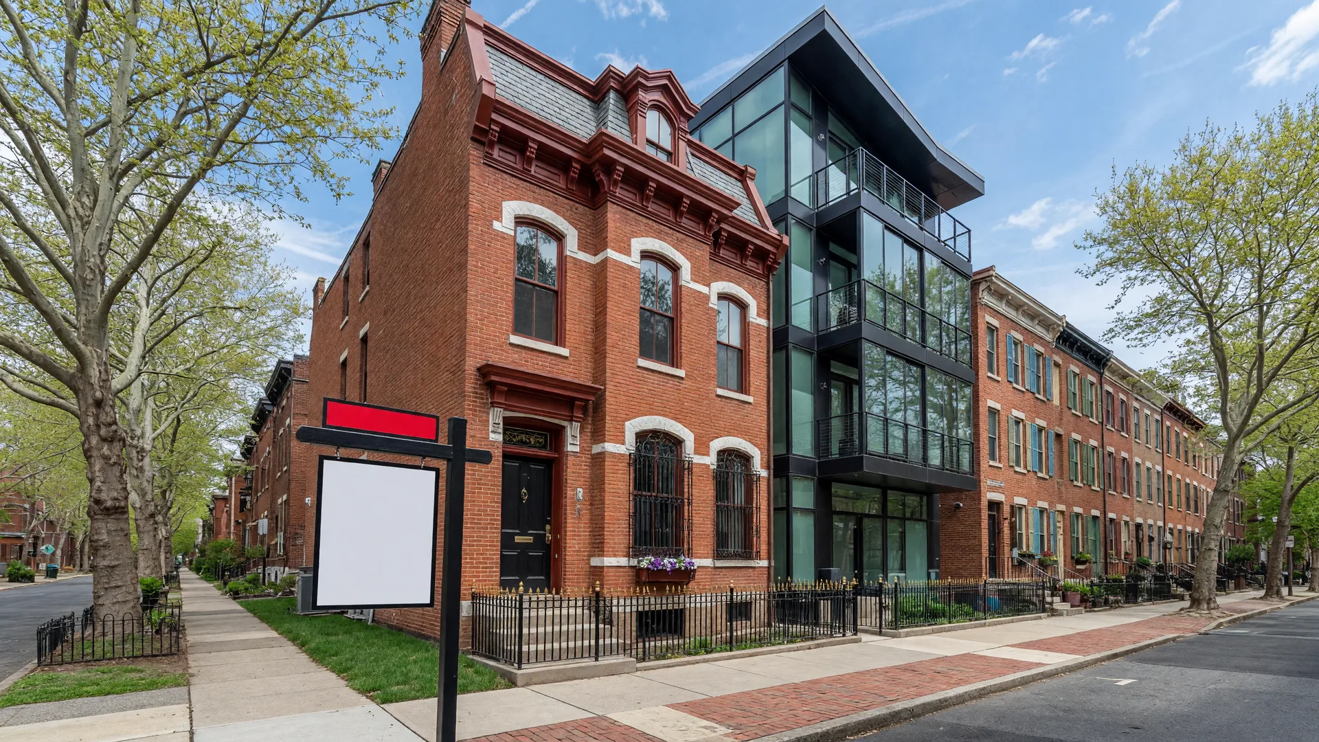 For Sale sign in front of a restored historic Philadelphia rowhome in Graduate Hospital with a modern condo building visible down the street