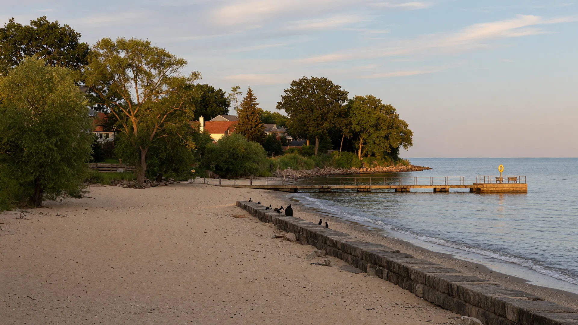 Golden-hour view of Huntington Beach on the Lake Erie shoreline in Bay Village, Ohio, with sand, breakwall,and shoreline trees