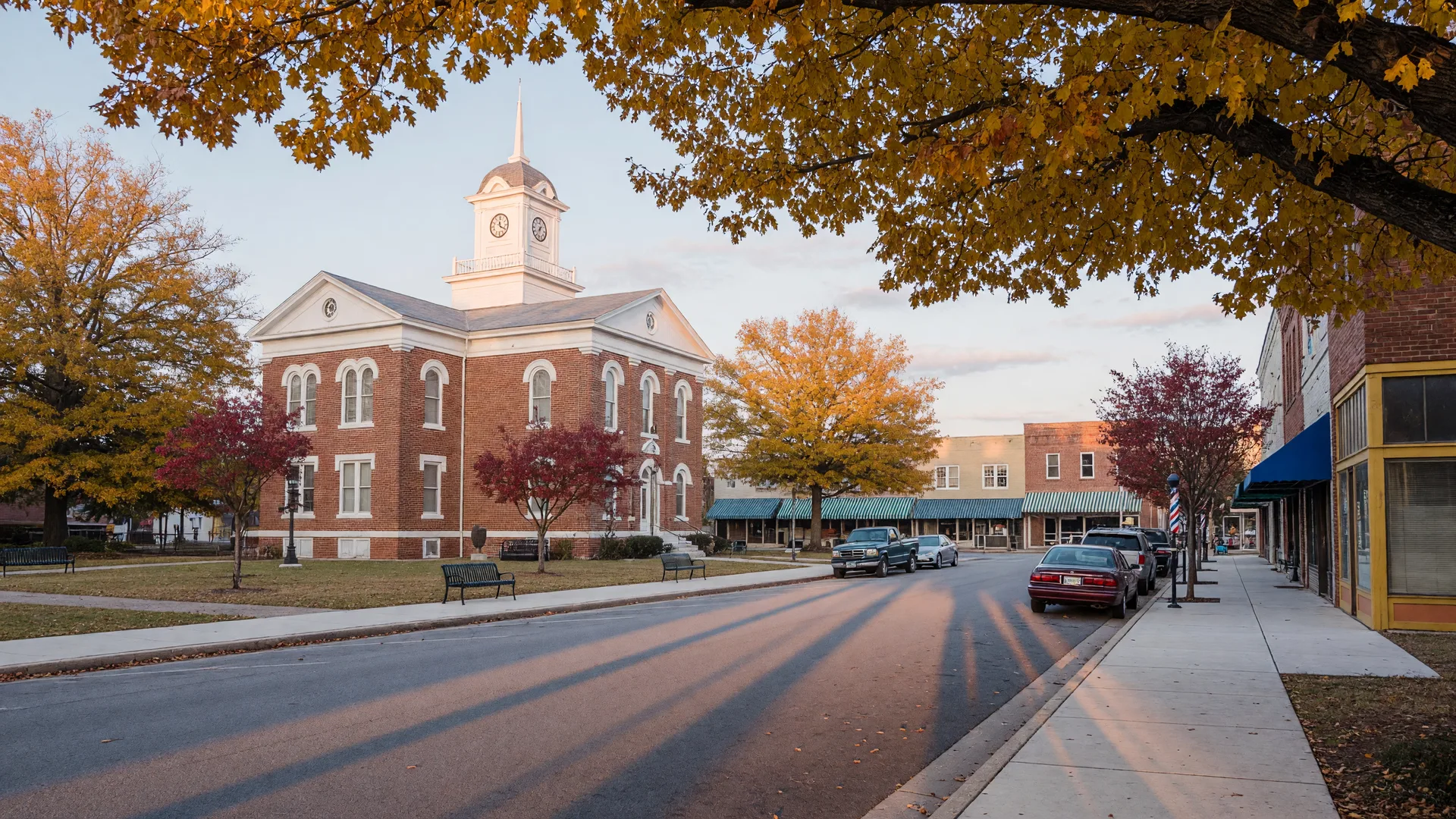 Hartwell's courthouse square on a crisp autumn morning: a historic brick courthouse with a white cupola framed by golden oaks and tidy storefronts