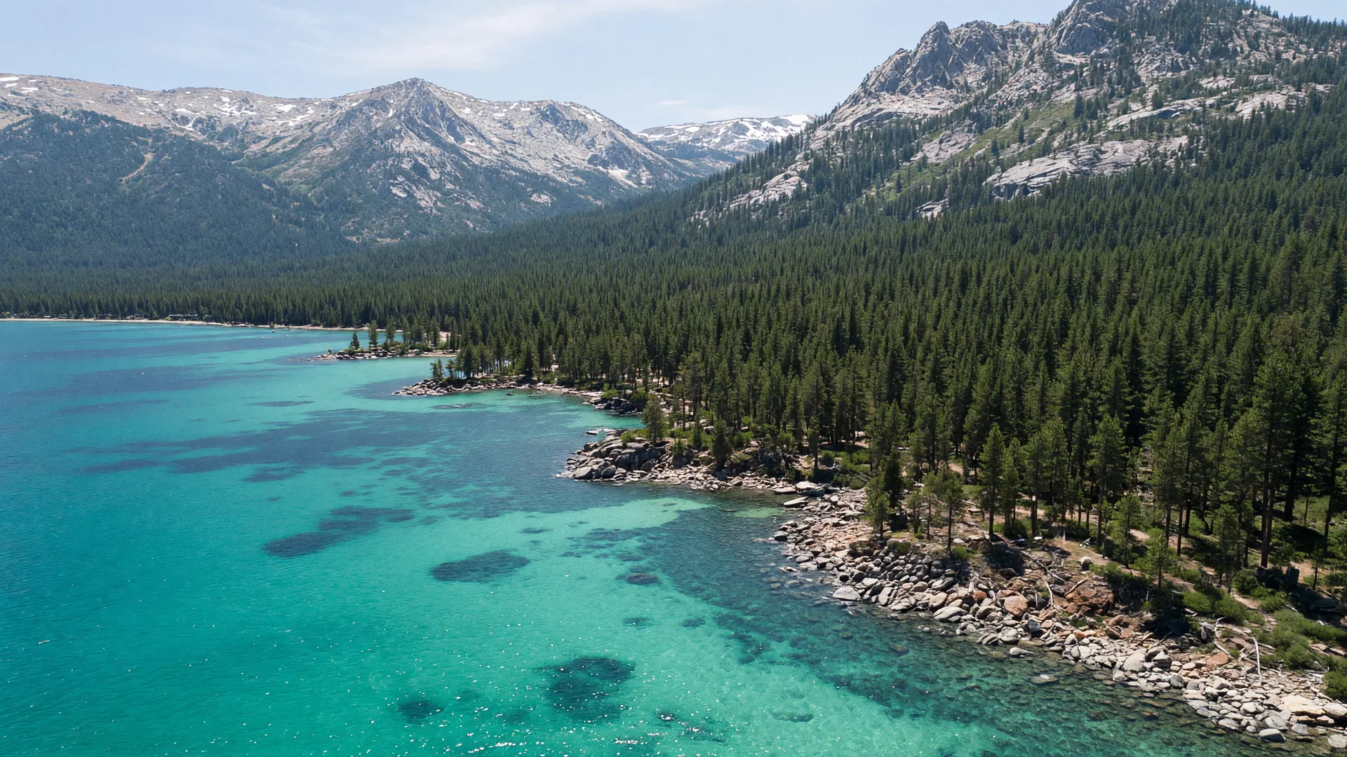 Aerial view of Lake Tahoe with turquoise water, rocky shoreline, and forested mountains.