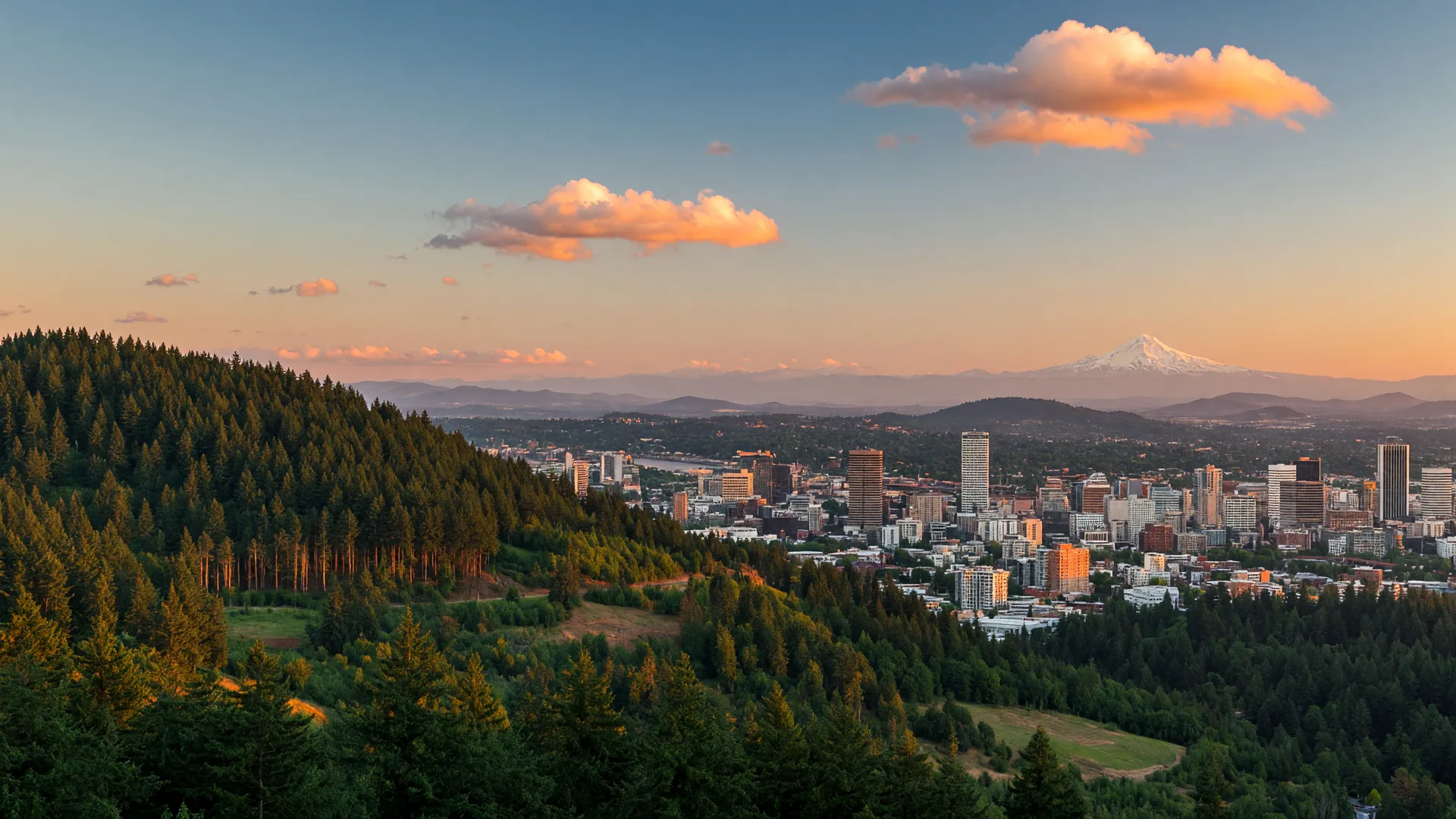 Portland Oregon downtown skyline with forested hills at golden hour anda faint Mount Hood on the horizon