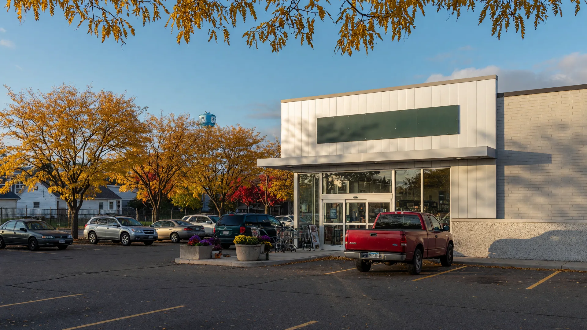 A modern grocery store in a small Minnesota town on a crisp October afternoon, with golden autumn trees along the parking lot