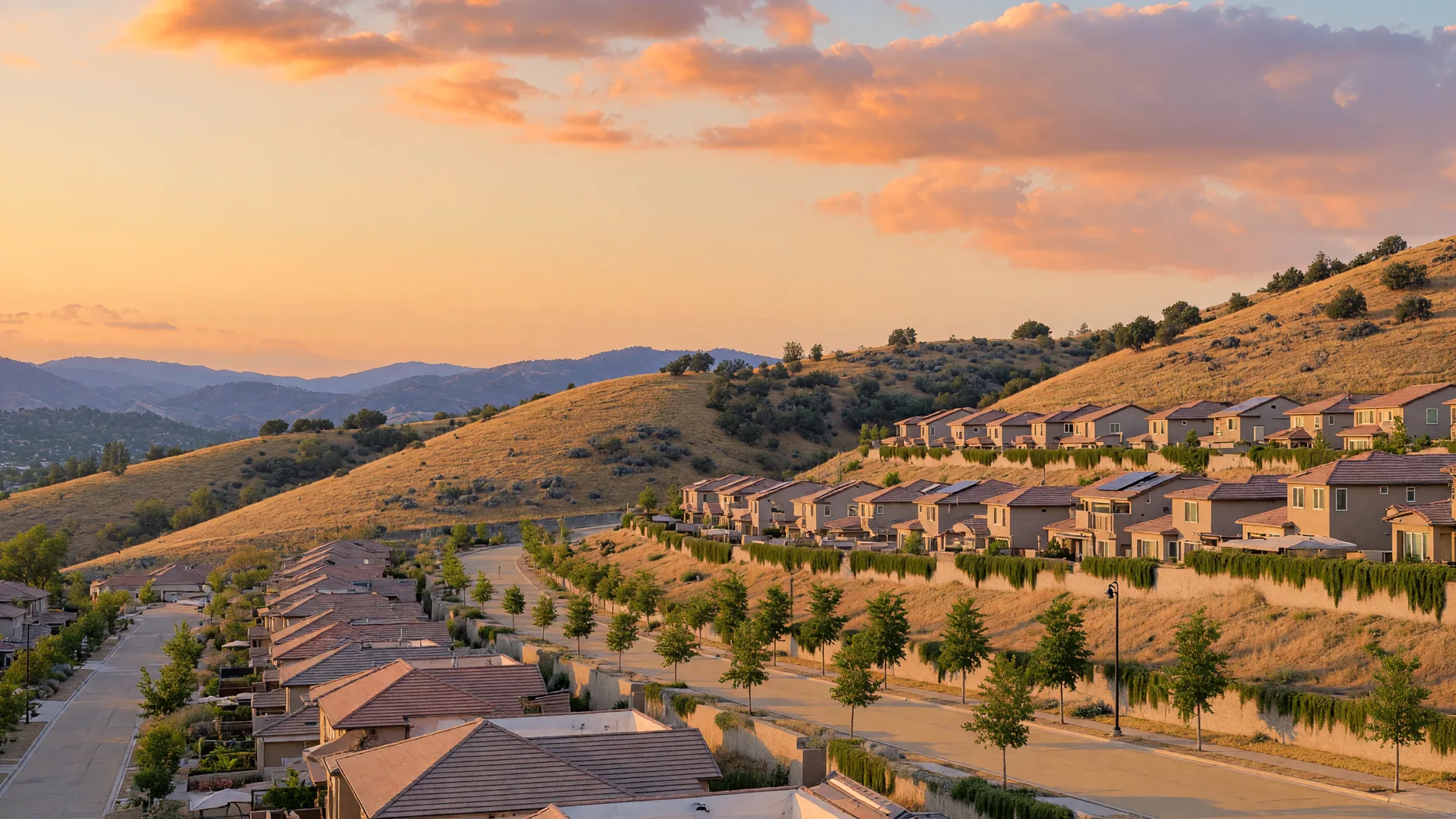 Village homes terraced into a sunlit California hillside under a big warm sky, grass rising to distant ridges