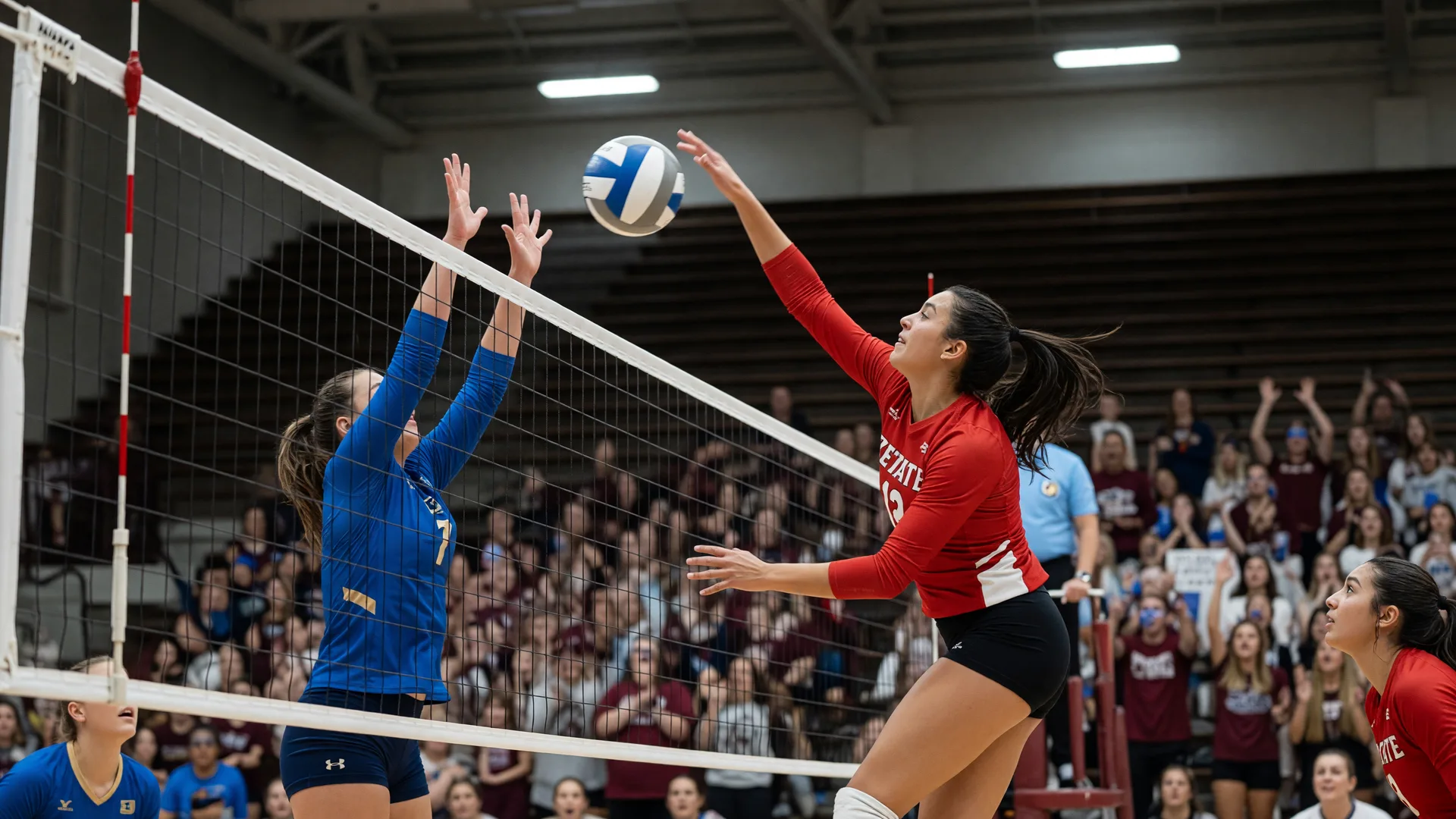 Two collegiate volleyball players mid-air at the net in a university arena with wood bleachers