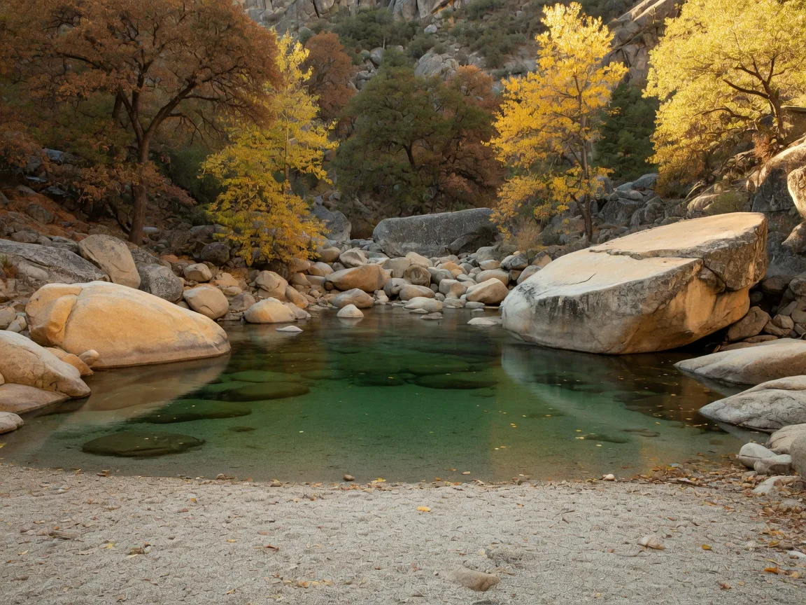 A free swimming hole on the Merced River in the Sierra foothills east of Mariposa on a late-October afternoon, a calm green-tinted pool between granite boulders, a small empty gravel beach, and golden cottonwoods and black oaks along the canyon walls