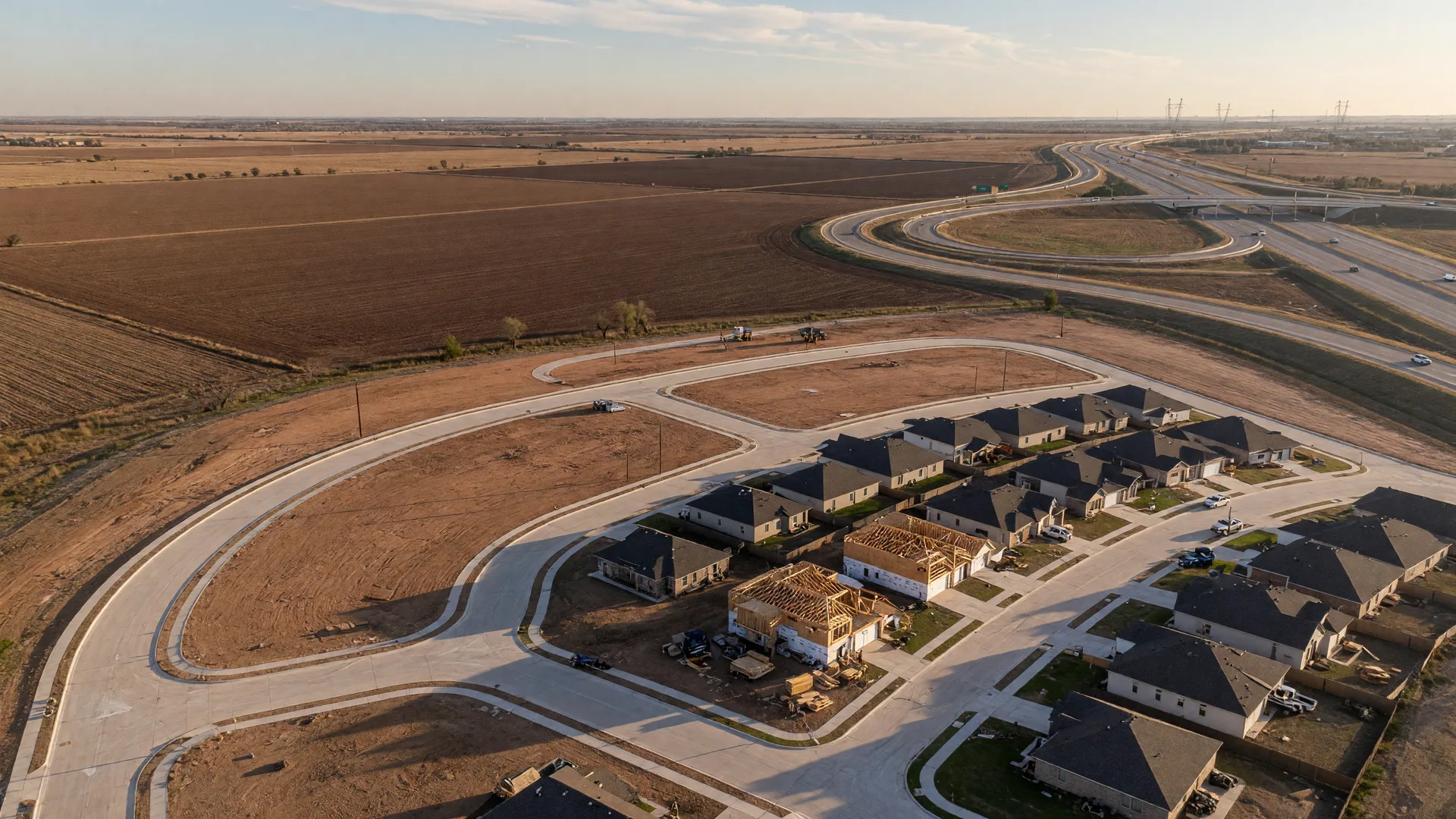 Aerial view of a new North Texas development with paved streets near farmland and a distant highway interchange on the FM 407 corridor
