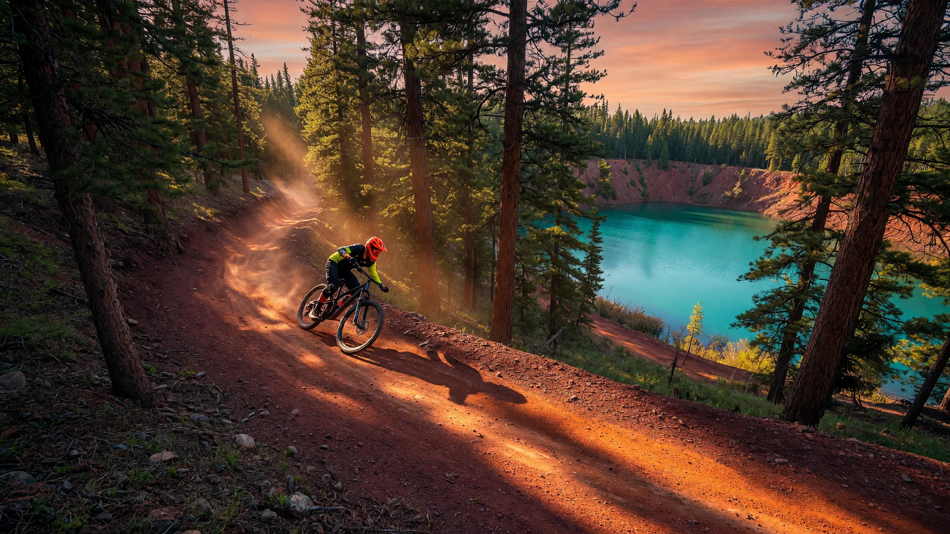 Mountain biker riding a red-gold trail through Cuyuna Country State Recreation Area with turquoise mine lake in the distance