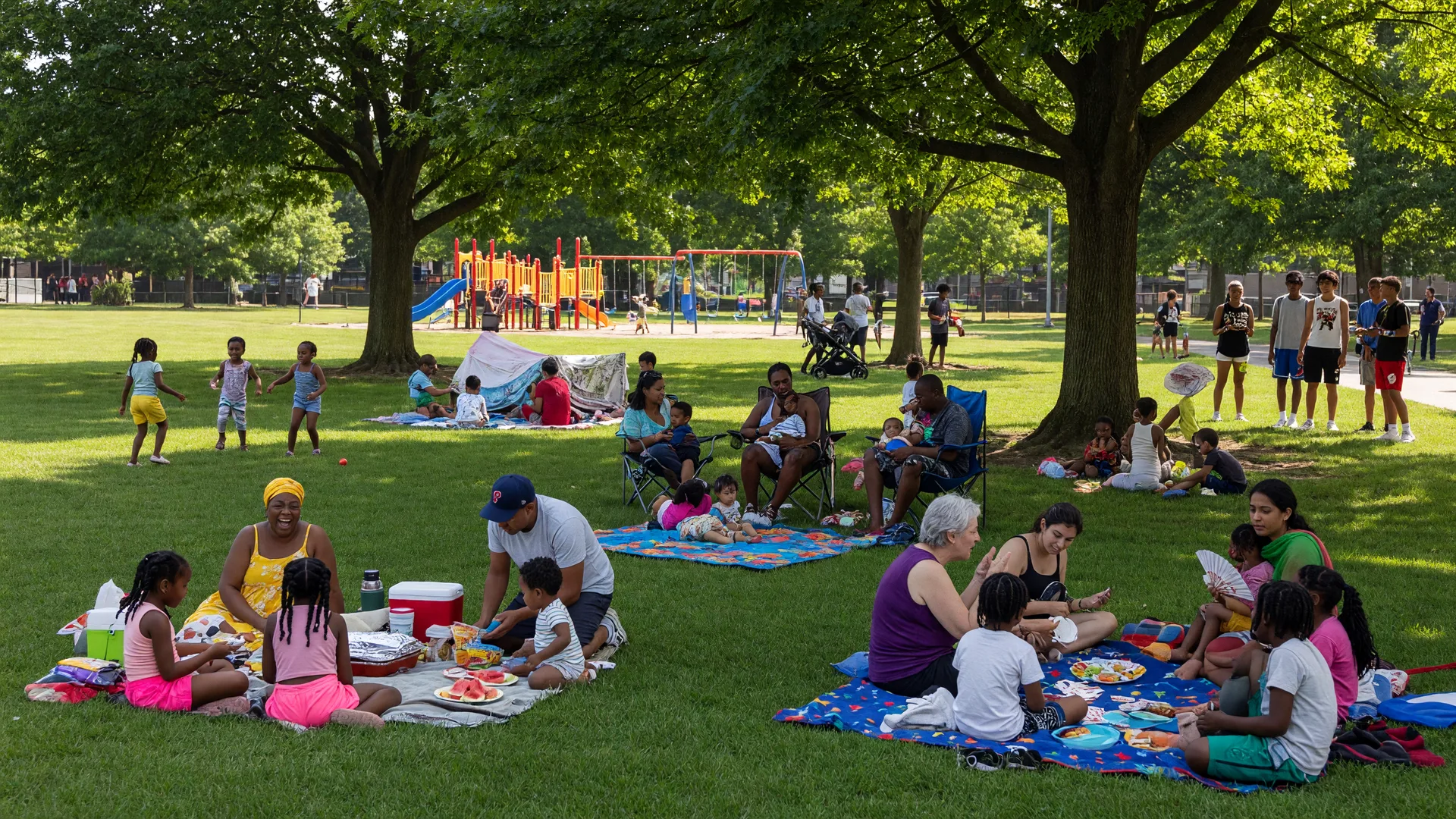 Community gathering at a park in Mt. Airy, Philadelphia with families on the lawn and a playground in the background