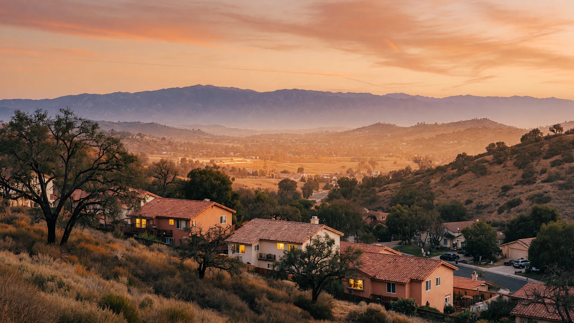 Hillside homes and terracotta roofs in the Santa Clarita Valley glowing in warm golden-hour light with mountains on the horizon