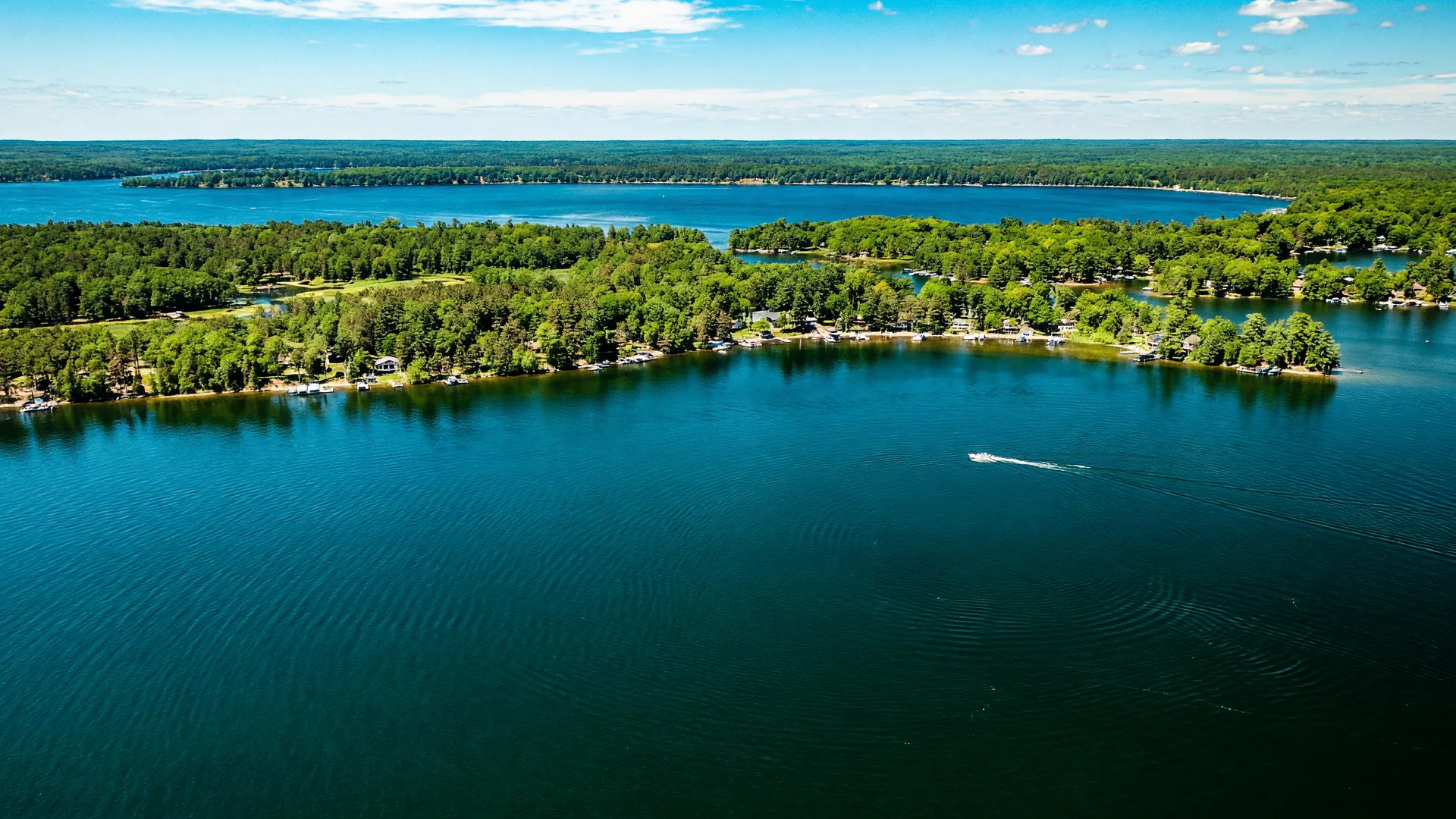 High-angle aerial view of a bright Minnesota lake surrounded by forest