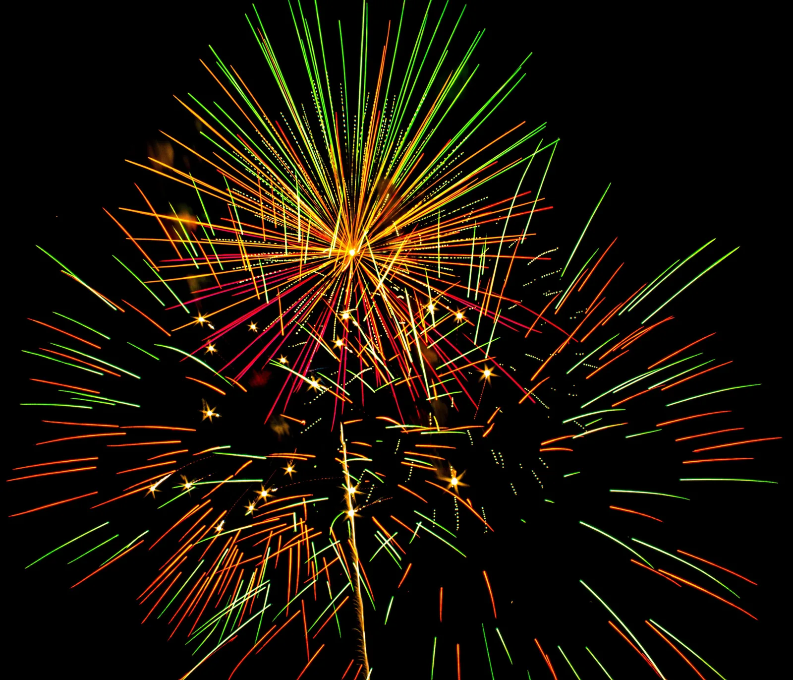 Festival scene with fireworks reflecting over water, vendor booths and community gathering visible in the foreground