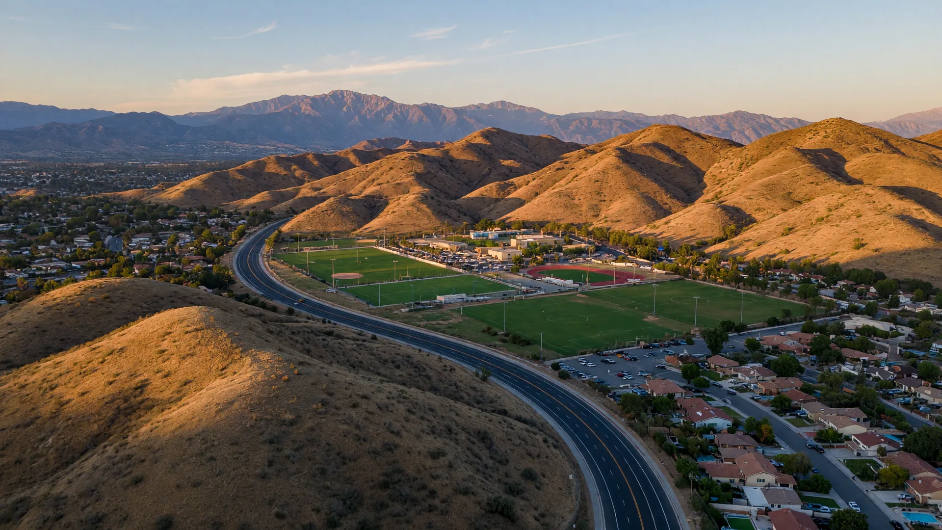 Golden chaparral hillsides in Canyon Country with a winding road and the Santa Clarita Sports Complex in the distance