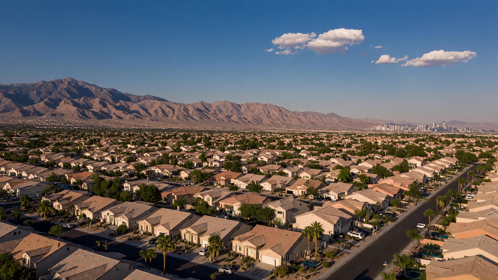 Aerial view of Las Vegas suburban neighborhoods at golden hour with tile-roof homes, palm trees, and the Spring Mountains on the horizon