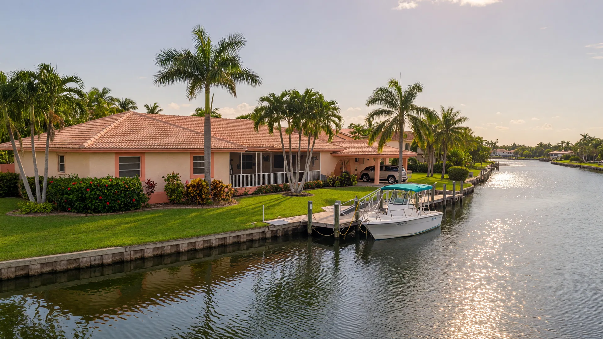 A canal-front Cape Coral home with a private boat dock, palms, a moored boat, and sunlight on the water