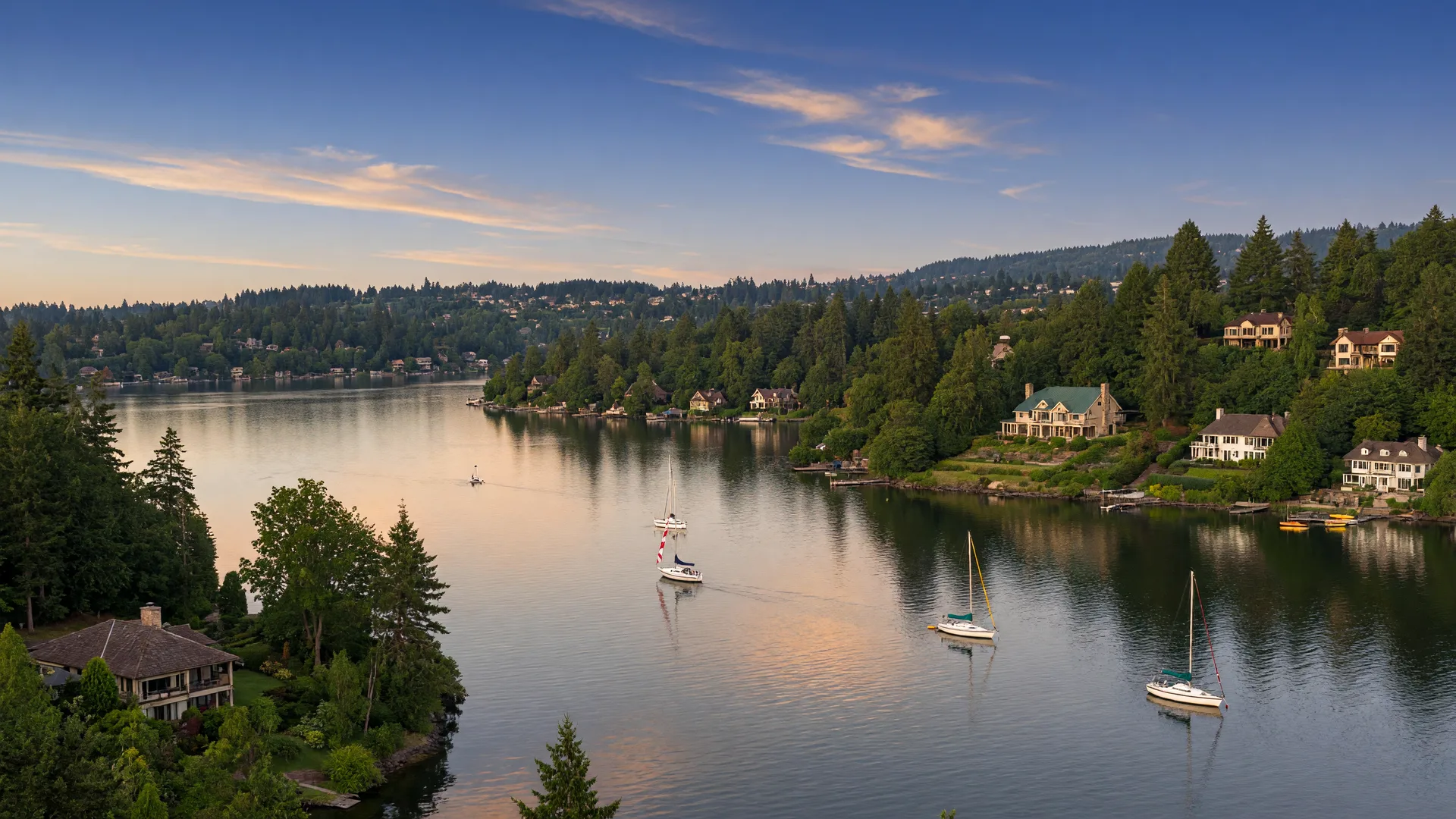 Oswego Lake at golden hour with sailboats on calm water and wooded hillsides beyond