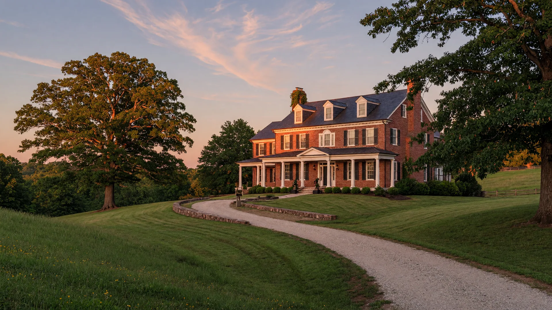 An elegant traditional brick home with white columns on a green hillside in the mid-Atlantic countryside at golden hour