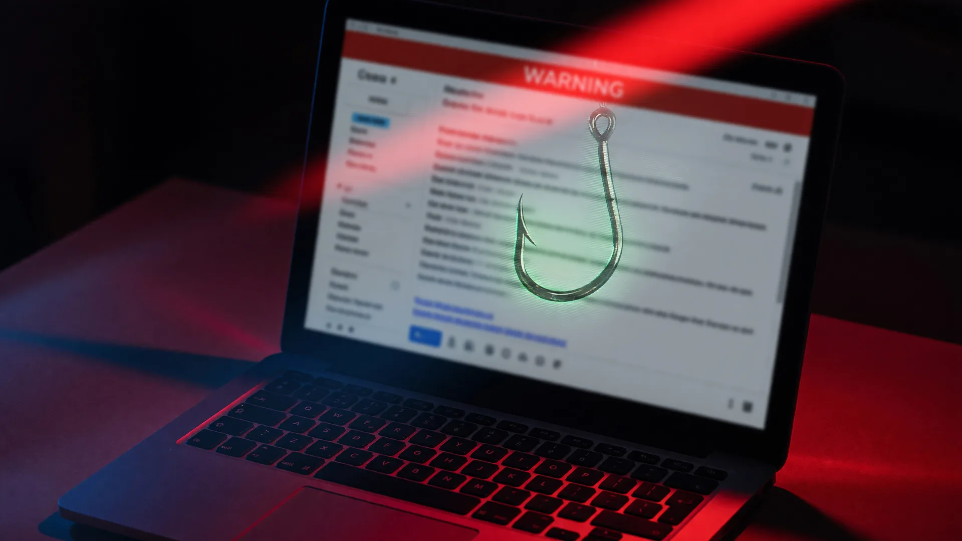 Laptop screen showing a phishing email with a glowing hook icon reflection in red warning light