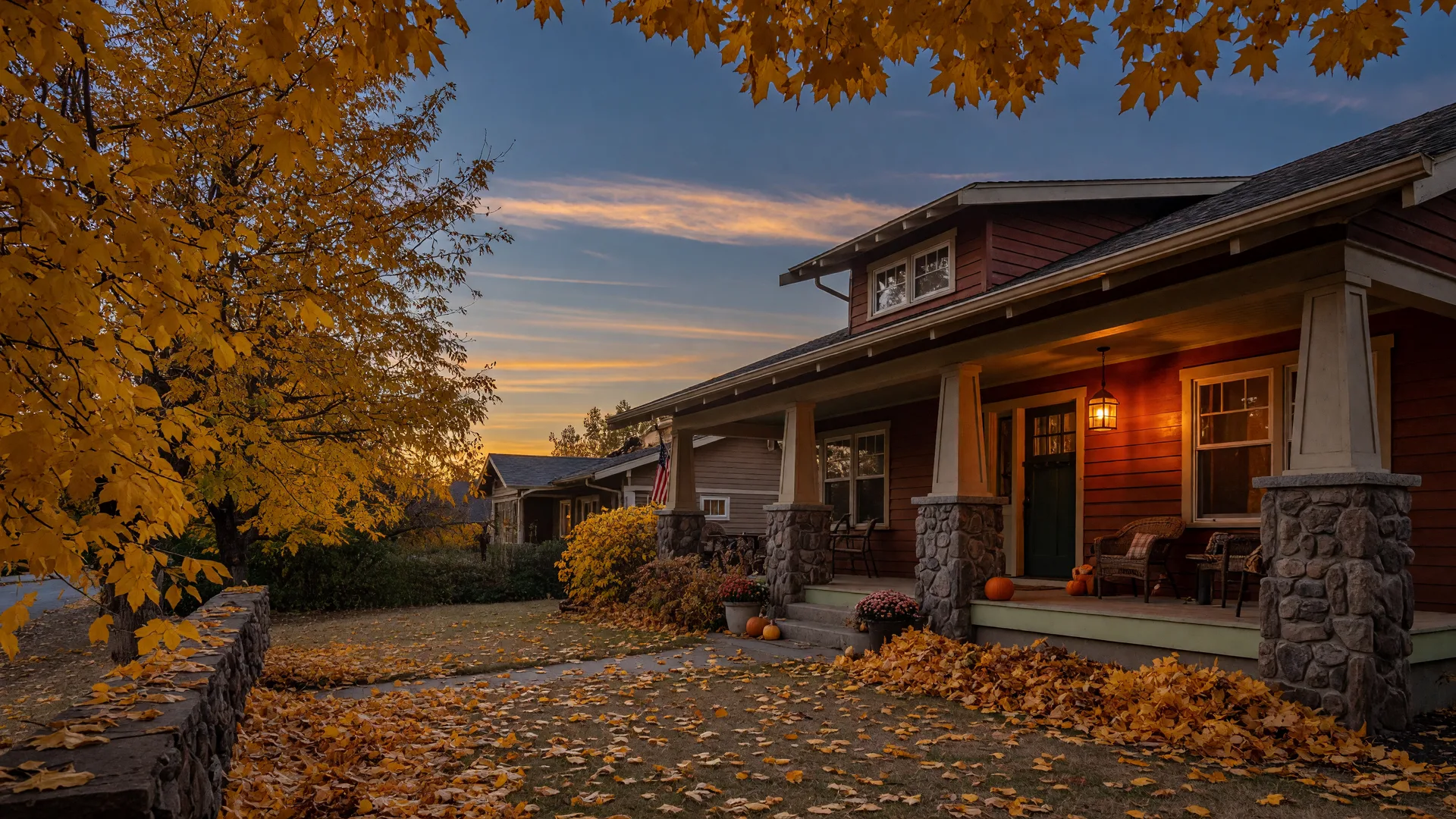 A warm craftsman home in the Tri-Cities with cedar siding and stone porch columns in late October light, golden leaves blanketing the yard and a lantern glowing on the porch