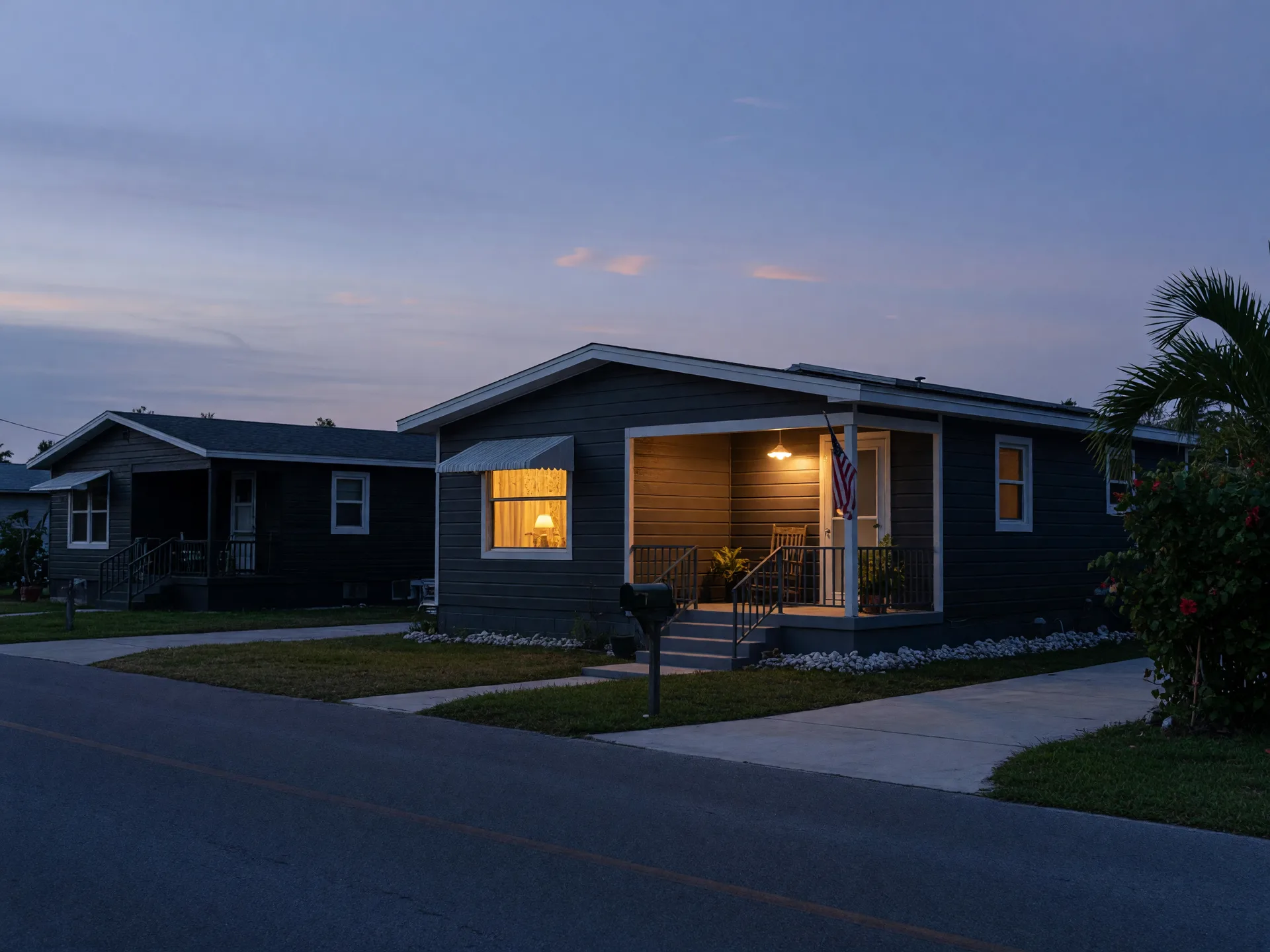 A quiet Florida street at blue hour with one warmly lit window in a charcoal home